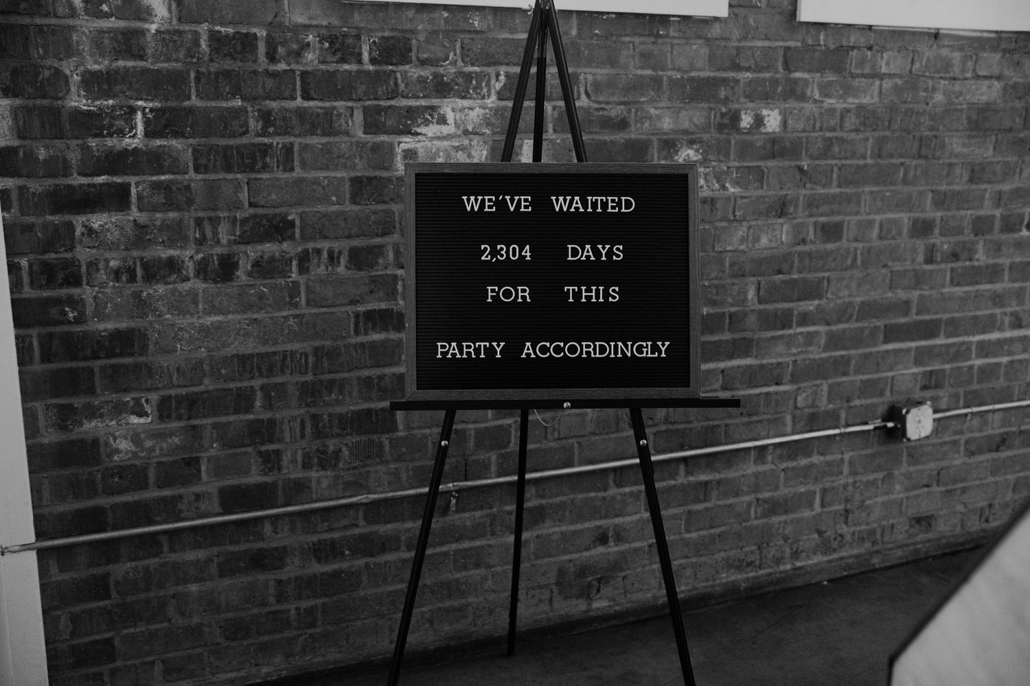 Black and white photo of a letterboard sign on an easel reading We've Waited 2,304 Days For This Party Accordingly.