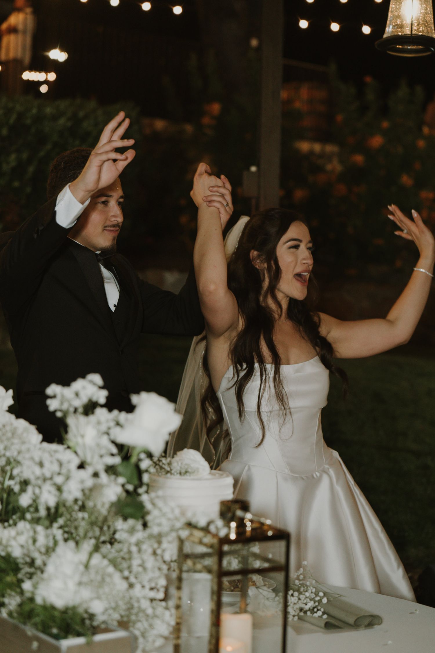 Wedding reception celebration with string lights and white floral decorations.