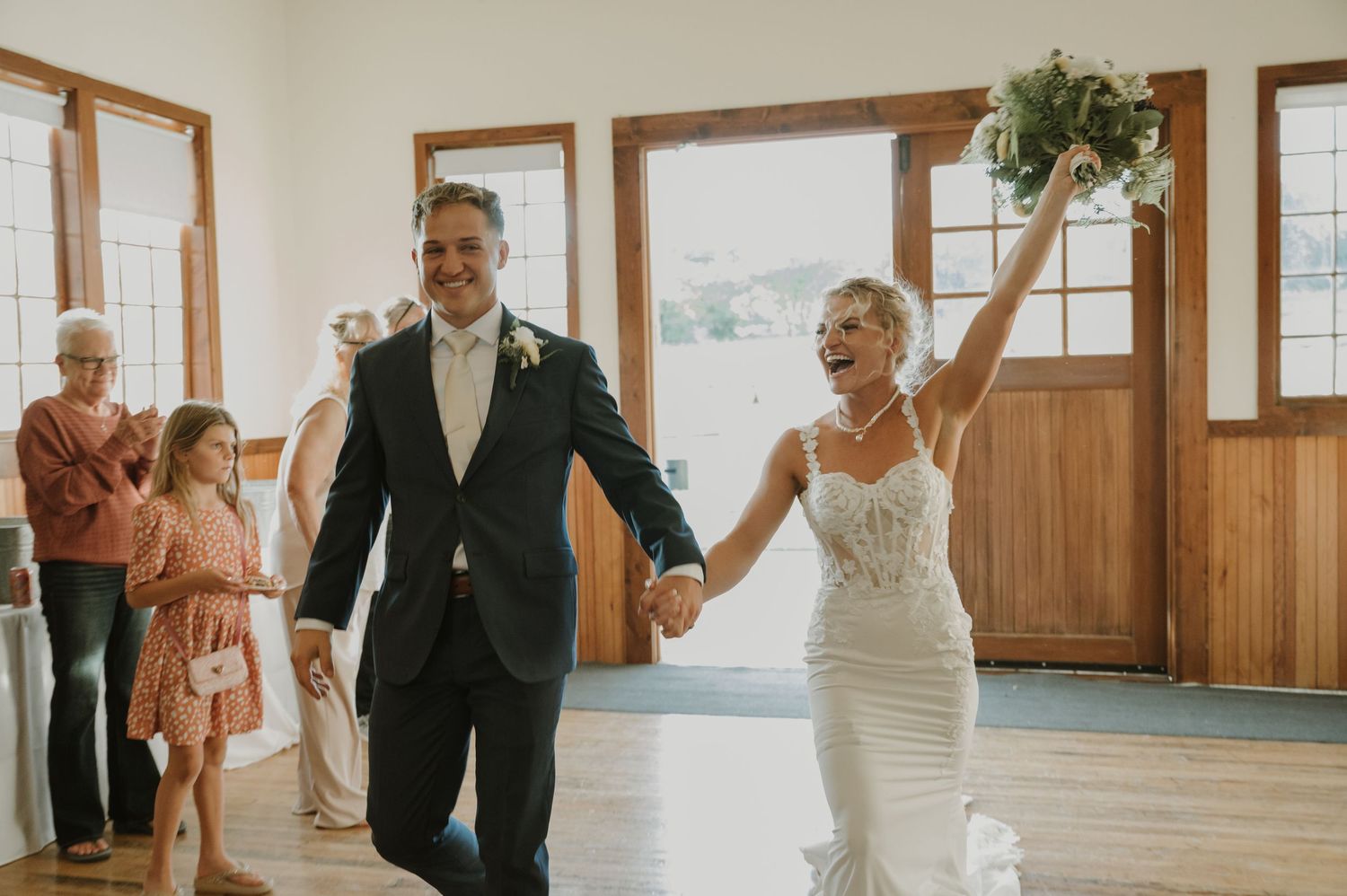 Wedding ceremony celebration in a rustic wooden venue with guests seated in white chairs.
