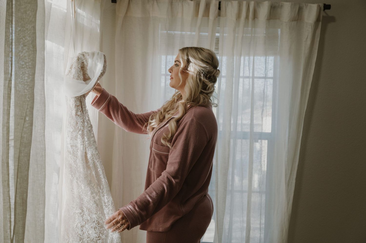 Artistic window light portrait with flowing curtains in muted tones.
