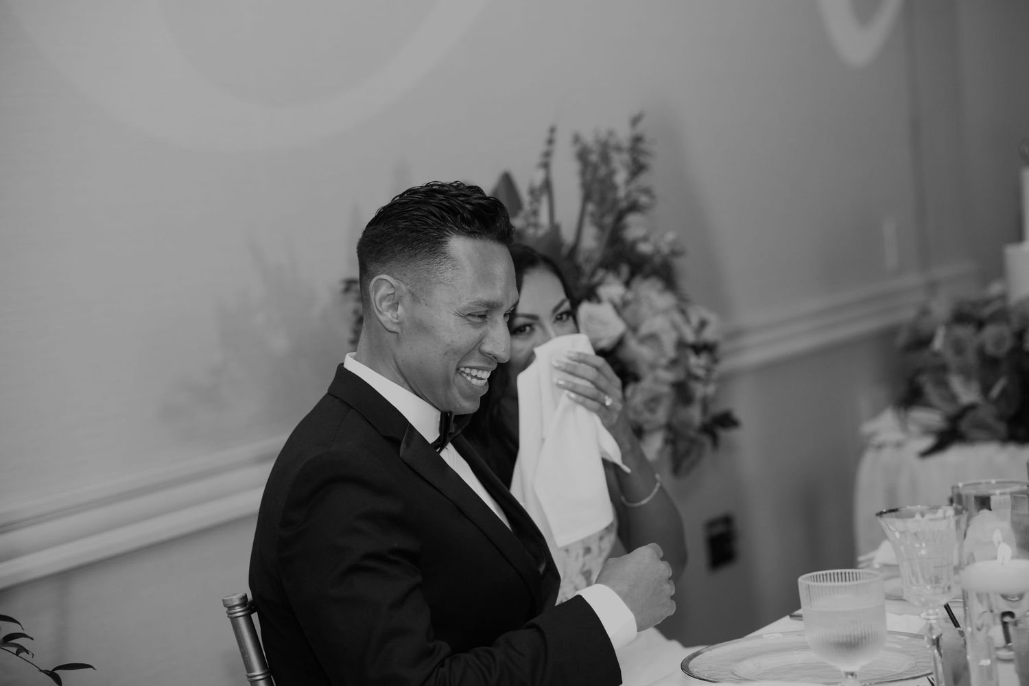 Wedding guests share joyful laughter and conversation during an elegant indoor reception.