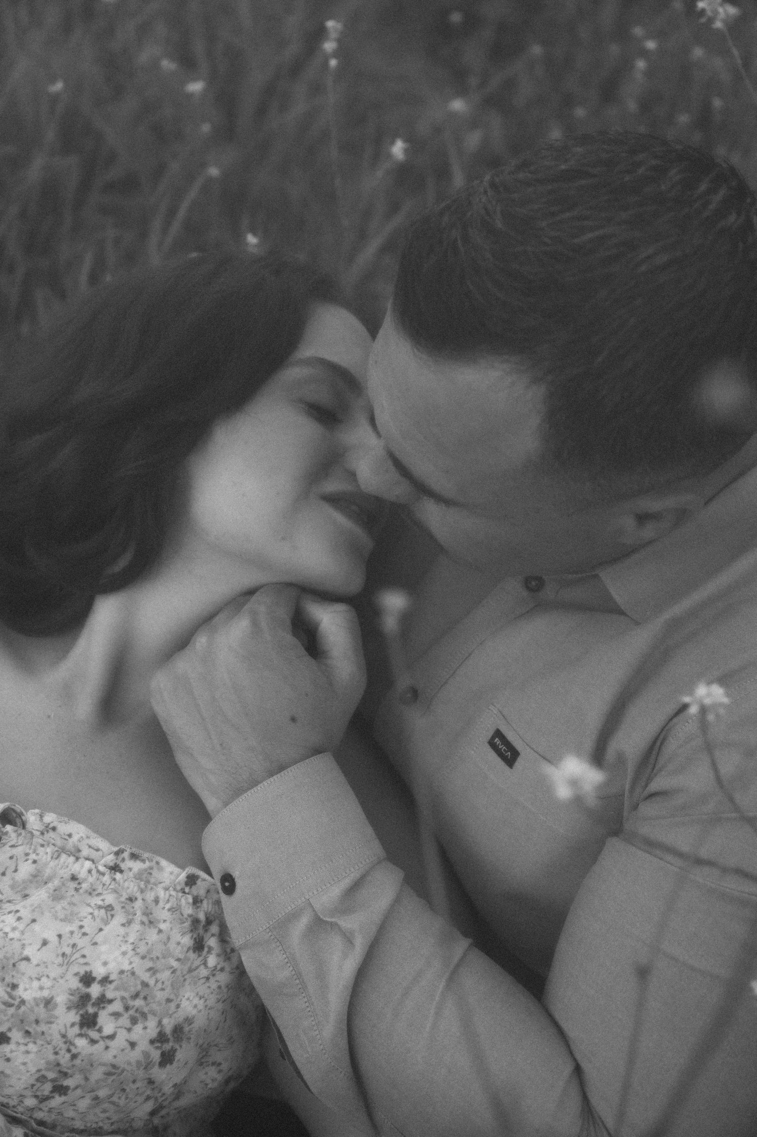 Black and white photo of a romantic couple sharing an intimate moment, almost kissing in a field of wildflowers.