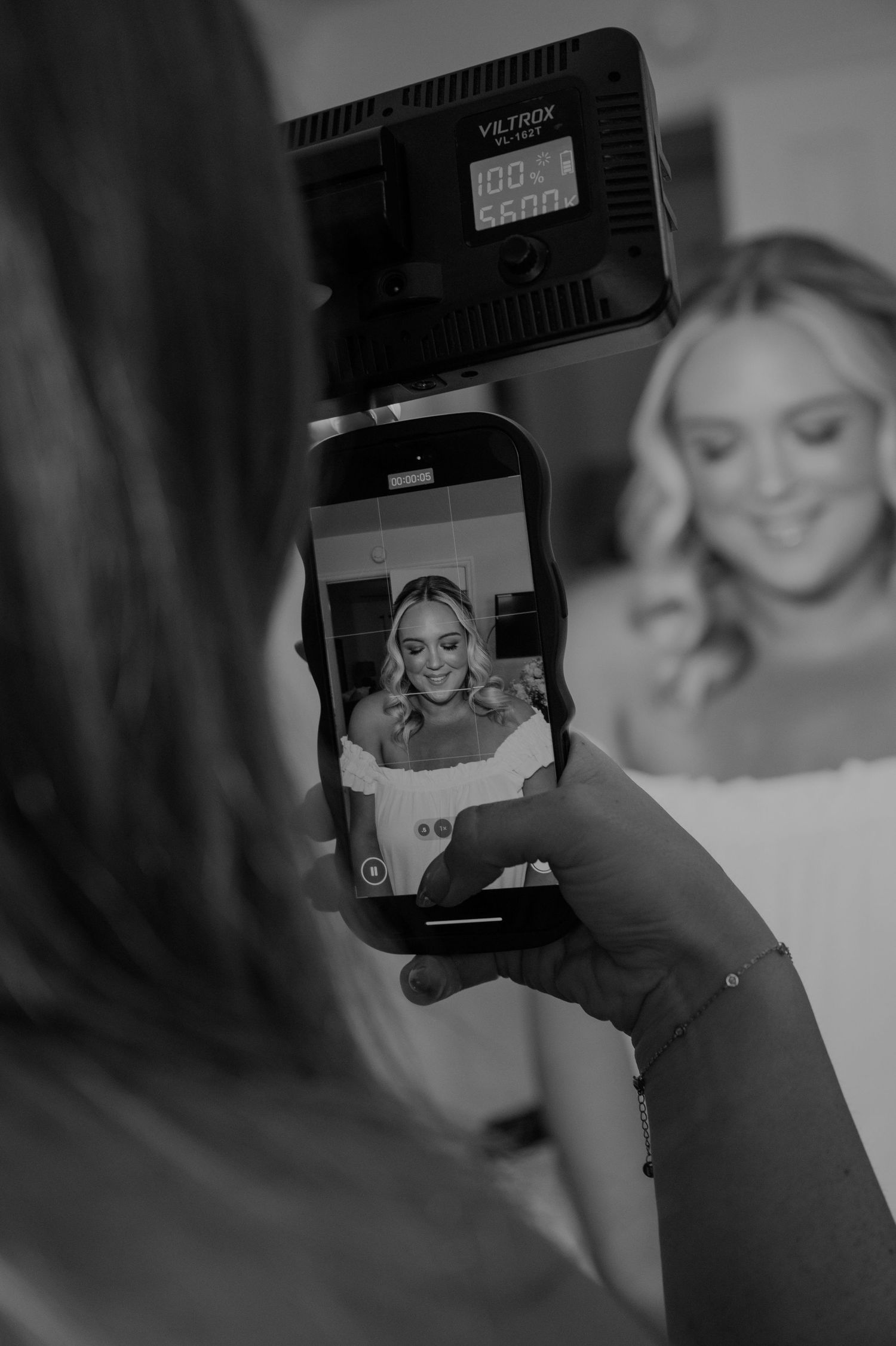 Photographer captures bride on smartphone with Viltrox light during wedding preparation in black and white.