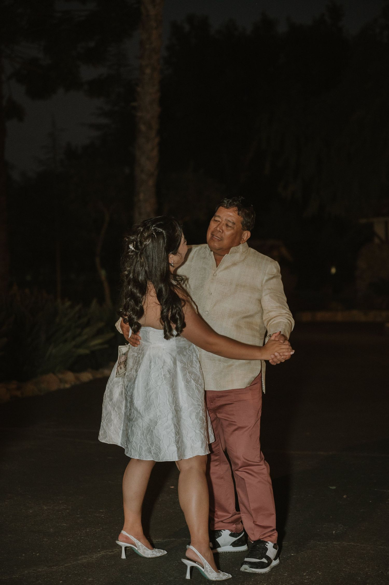 Couple sharing a dance outdoors at night during a wedding reception under dark skies.