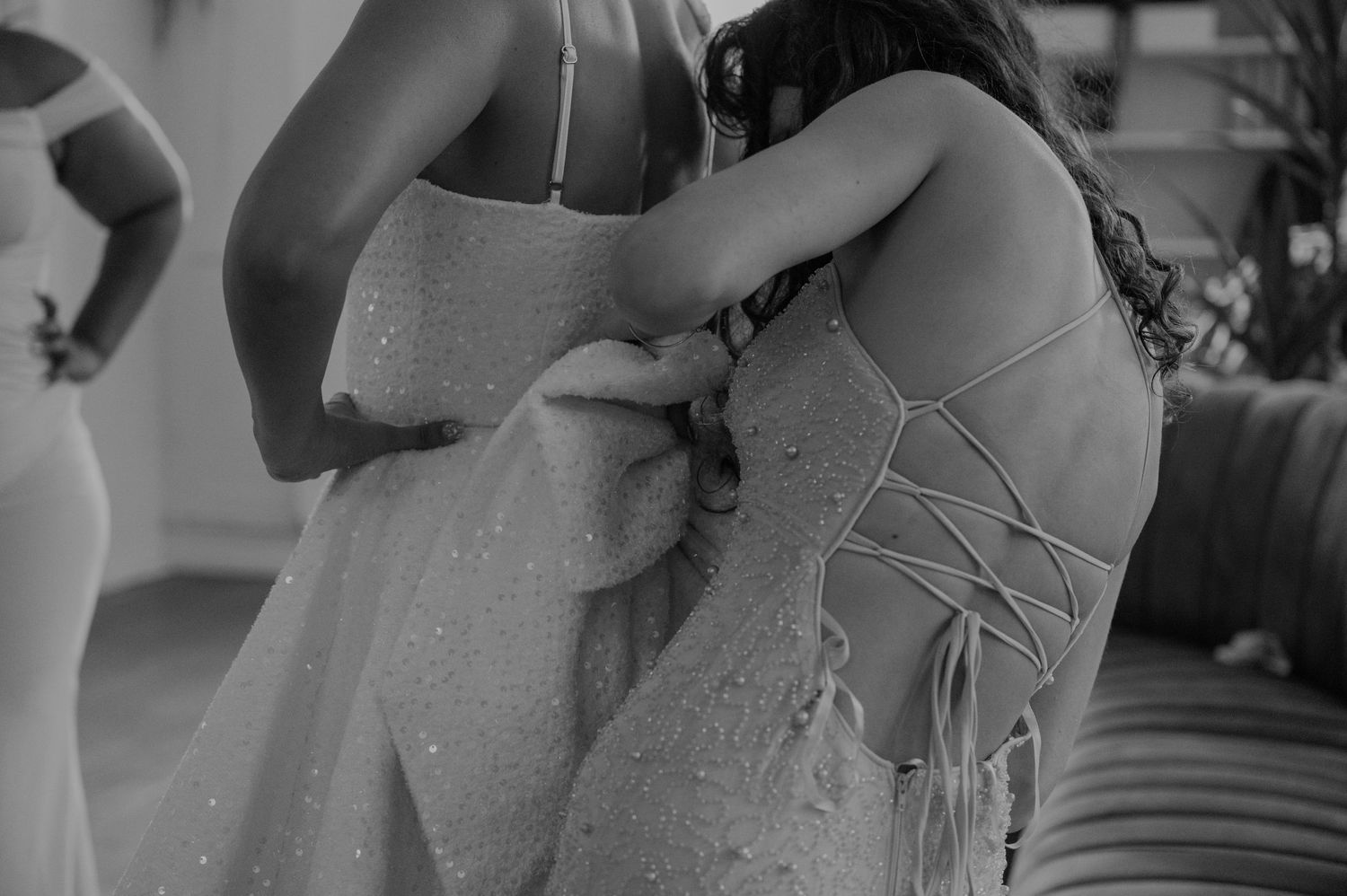 Black and white photo of bridesmaid helping bride lace up the back of her wedding dress.