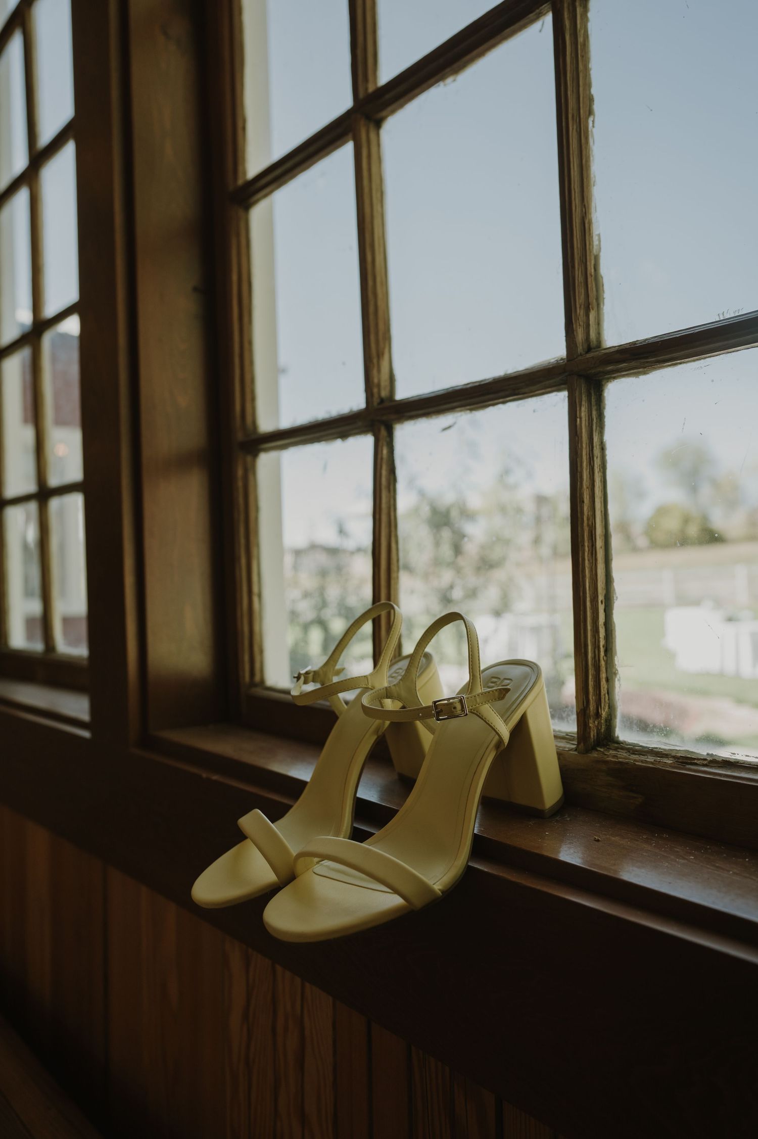 Cream-colored wedding heels displayed on a rustic windowsill with natural lighting.