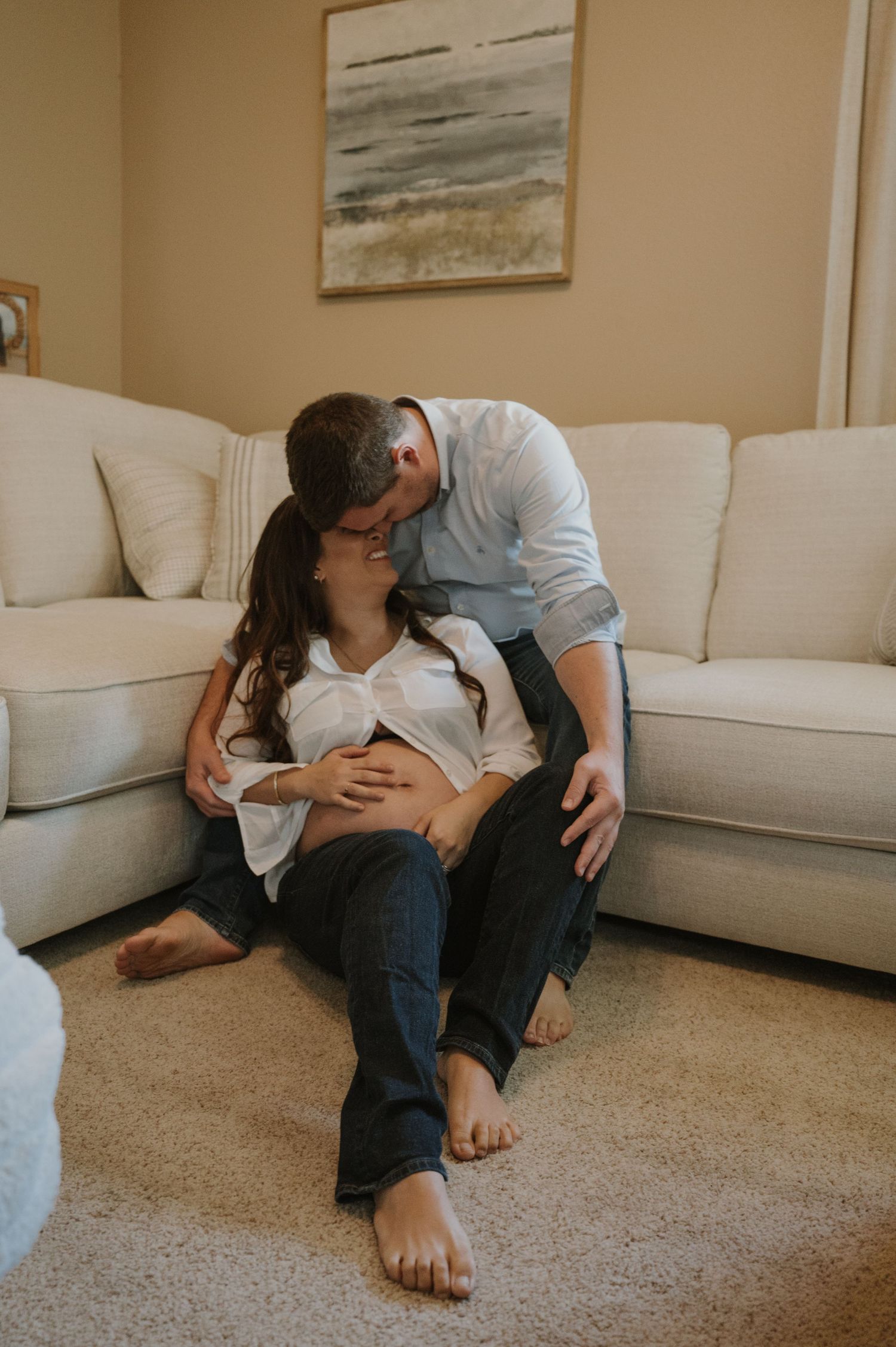 Intimate couple moment captured on a white couch in a living room with beige walls.