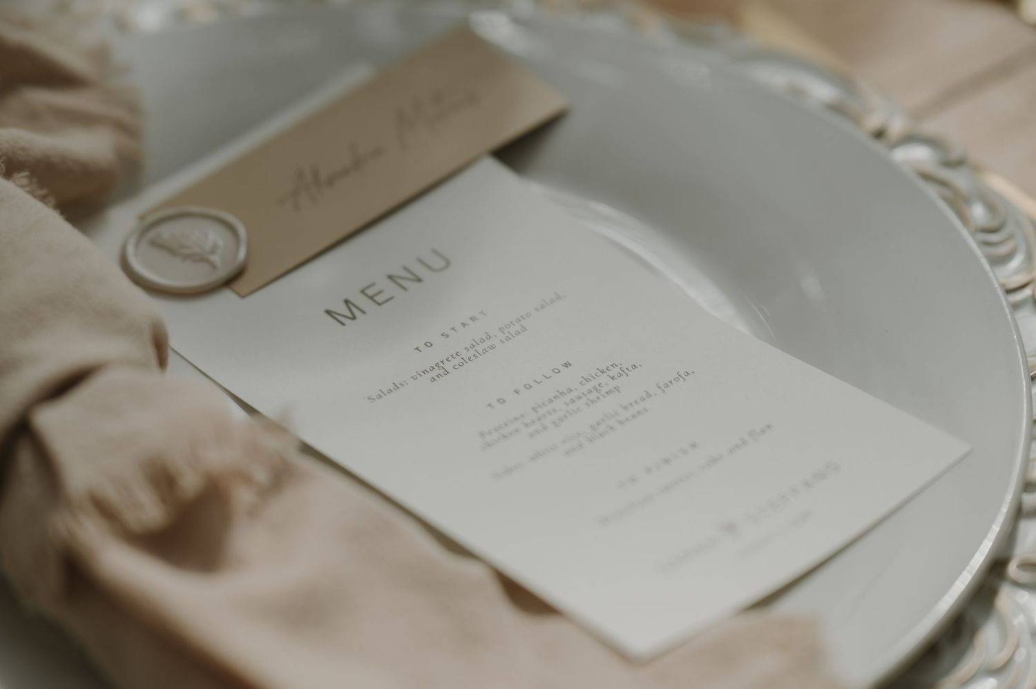 Minimalist wedding menu card on a white plate with a beige linen napkin and elegant name card.