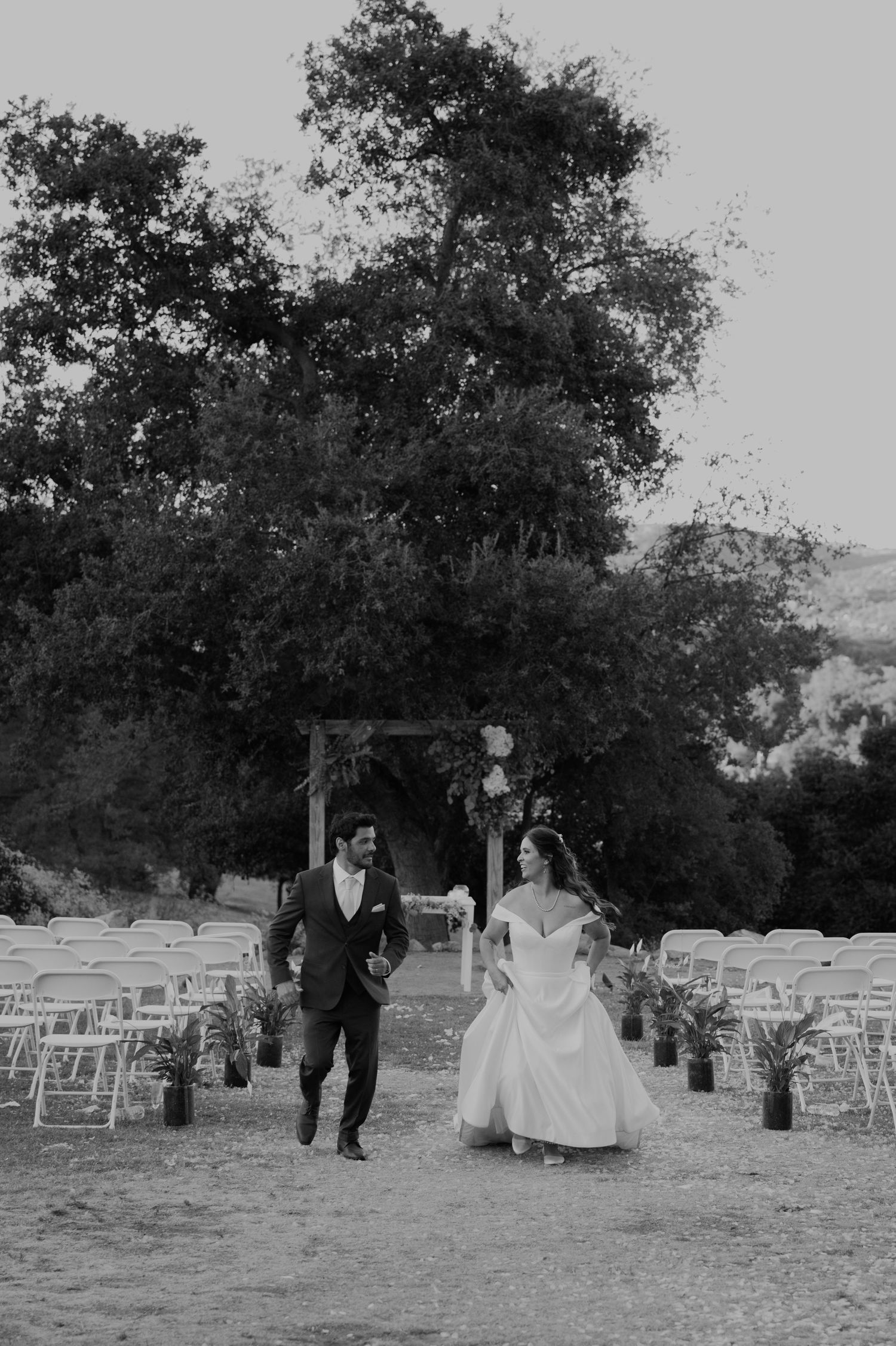 Black and white photo of a bride and groom walking down the aisle at an outdoor wedding ceremony.