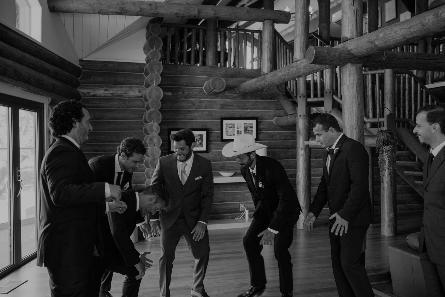 Groomsmen laughing and celebrating together in a rustic log cabin before a wedding ceremony.