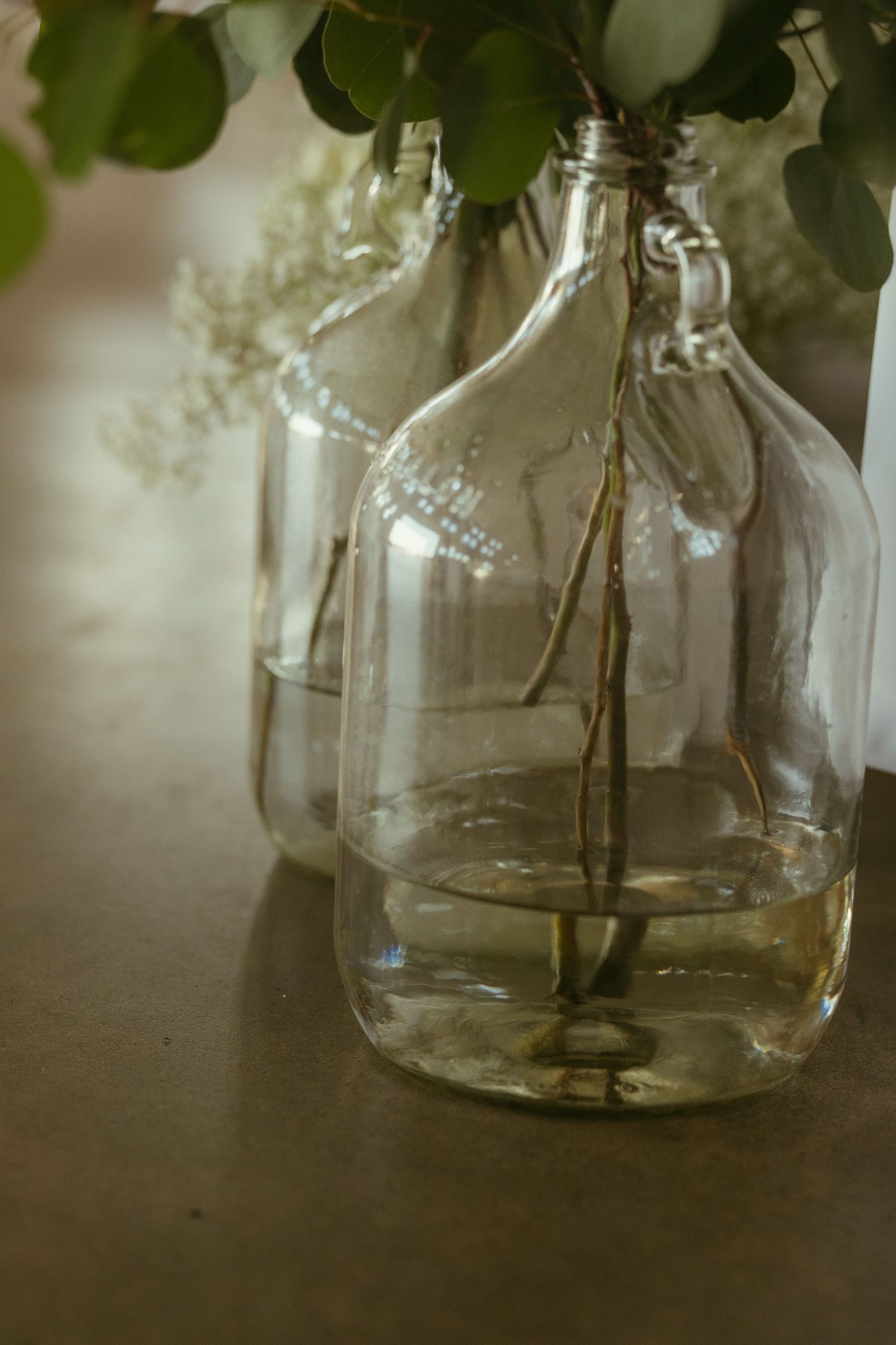 Clear glass bottle vases with fresh greenery and water on a rustic surface for elegant wedding decor.