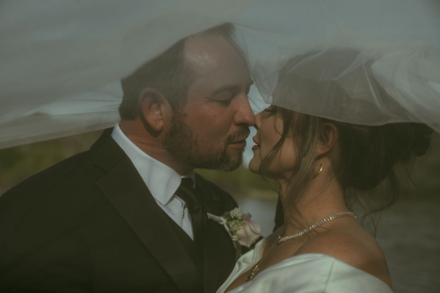 A bride and groom share a romantic kiss under a flowing white veil on their wedding day.