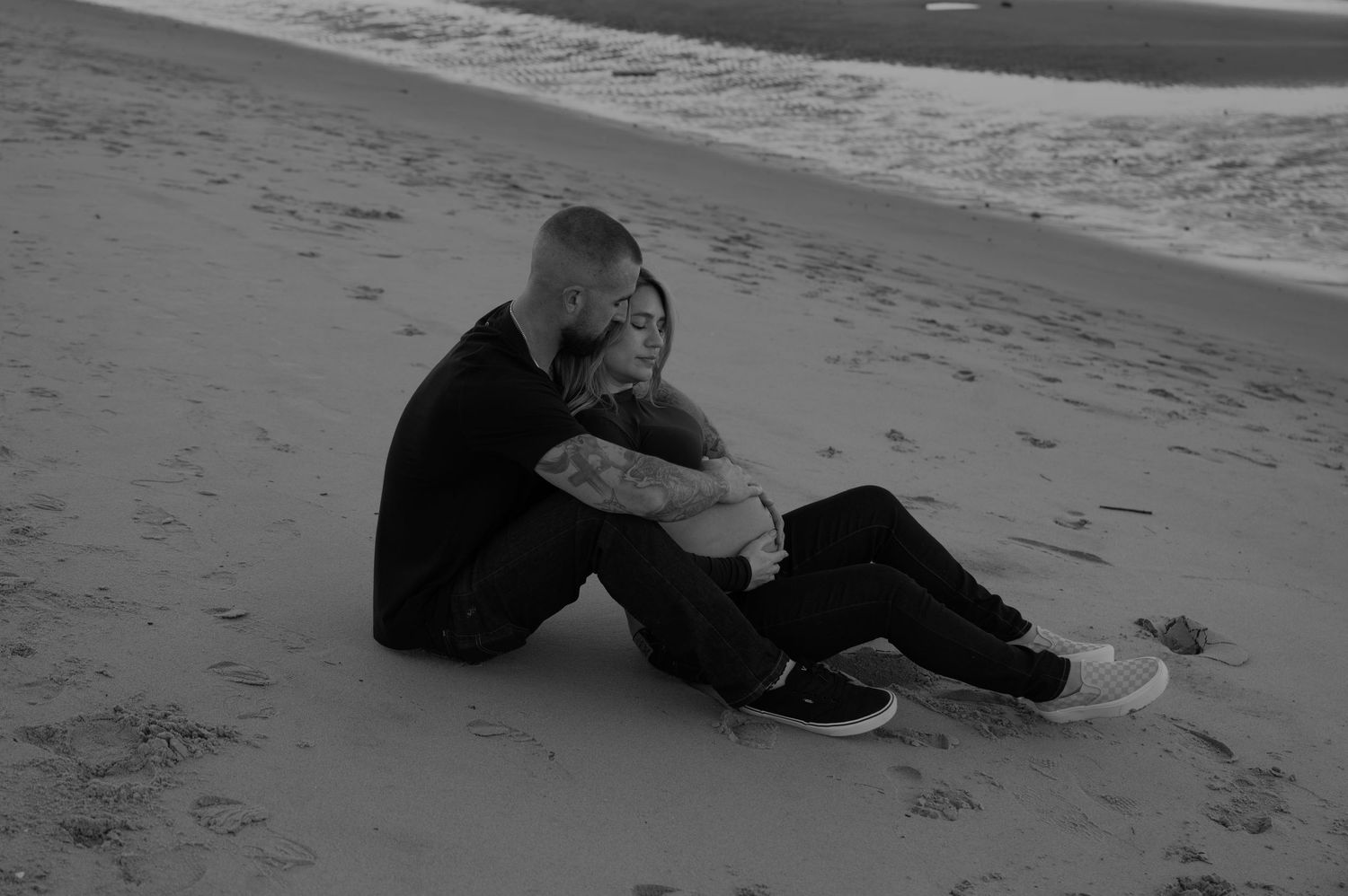 Two people sitting together on a beach in black and white.