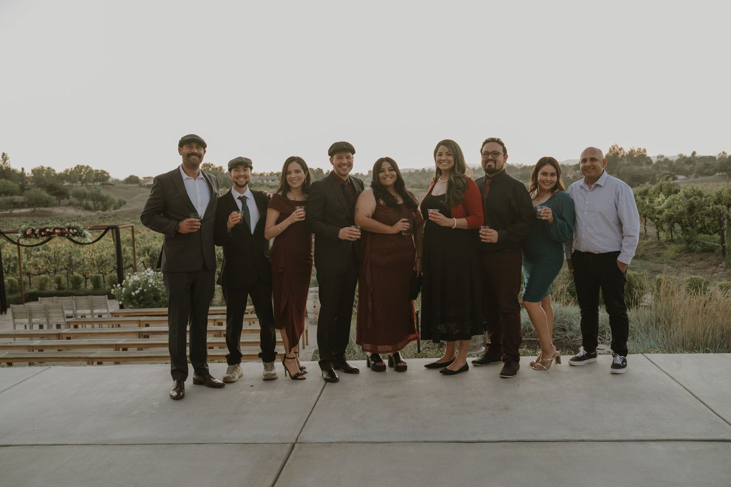 Wedding party lined up for group photos at outdoor vineyard venue.