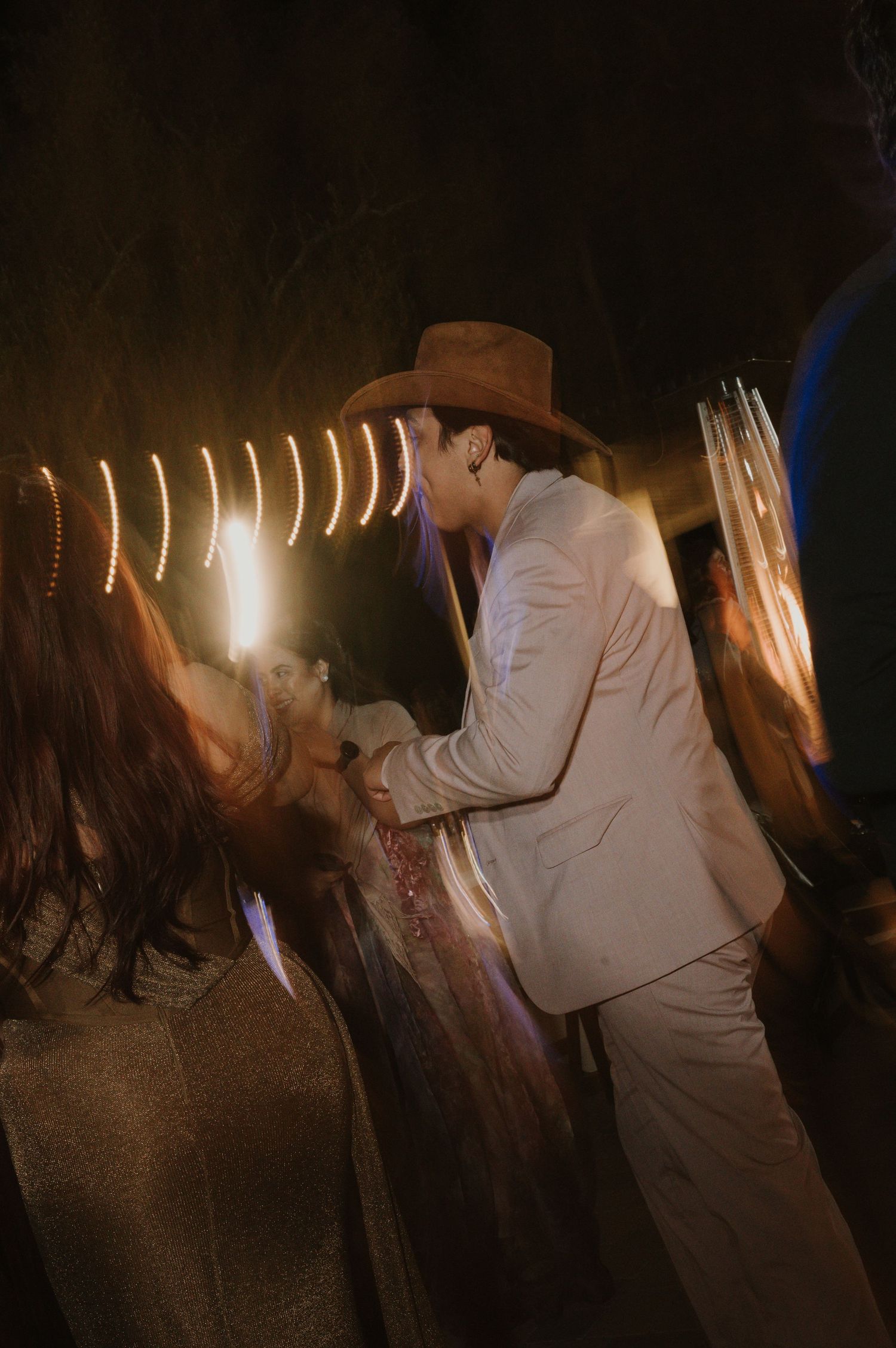 Wedding guests dance in a dimly lit venue with string lights overhead.