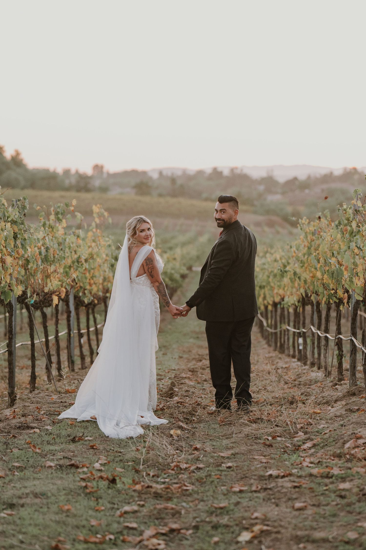 Newlyweds share intimate moment while walking through autumn vineyard.