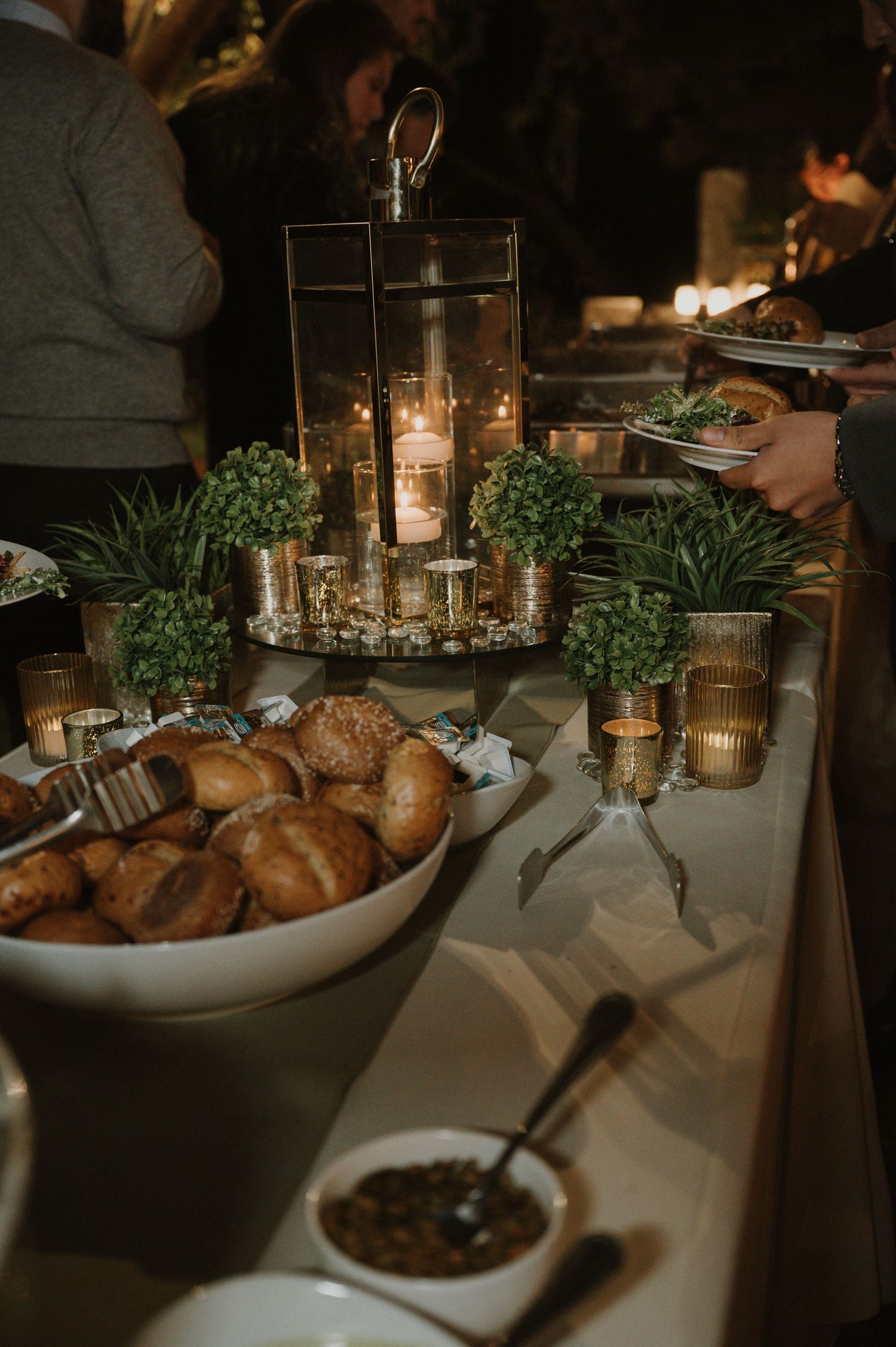 Candlelit buffet table with bread baskets and greenery decorations at an evening reception.