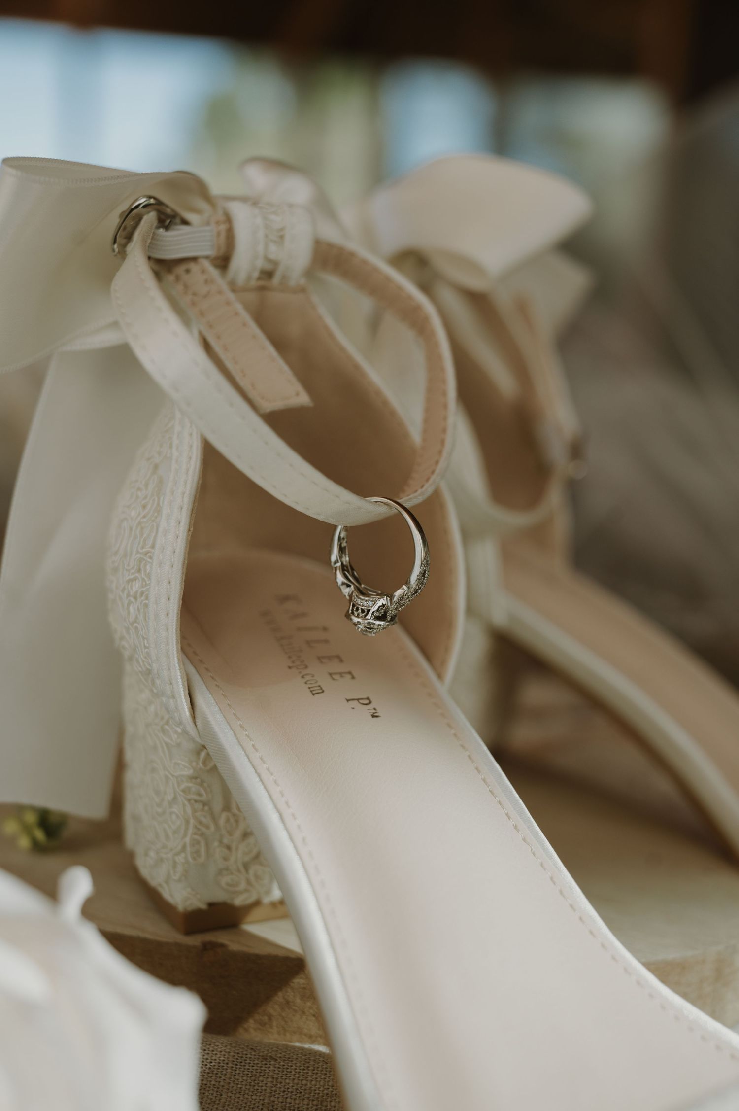 Elegant white wedding shoe with lace details and engagement ring balanced on the strap.
