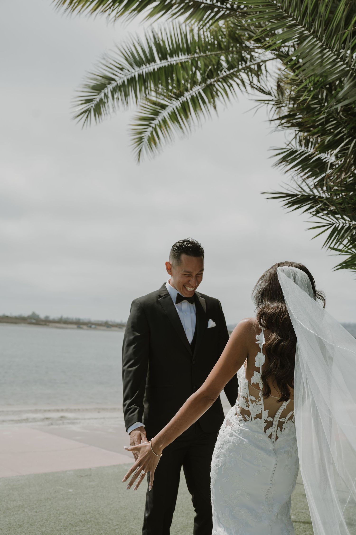 Beachfront wedding portraits under palm trees with ocean backdrop in soft lighting.