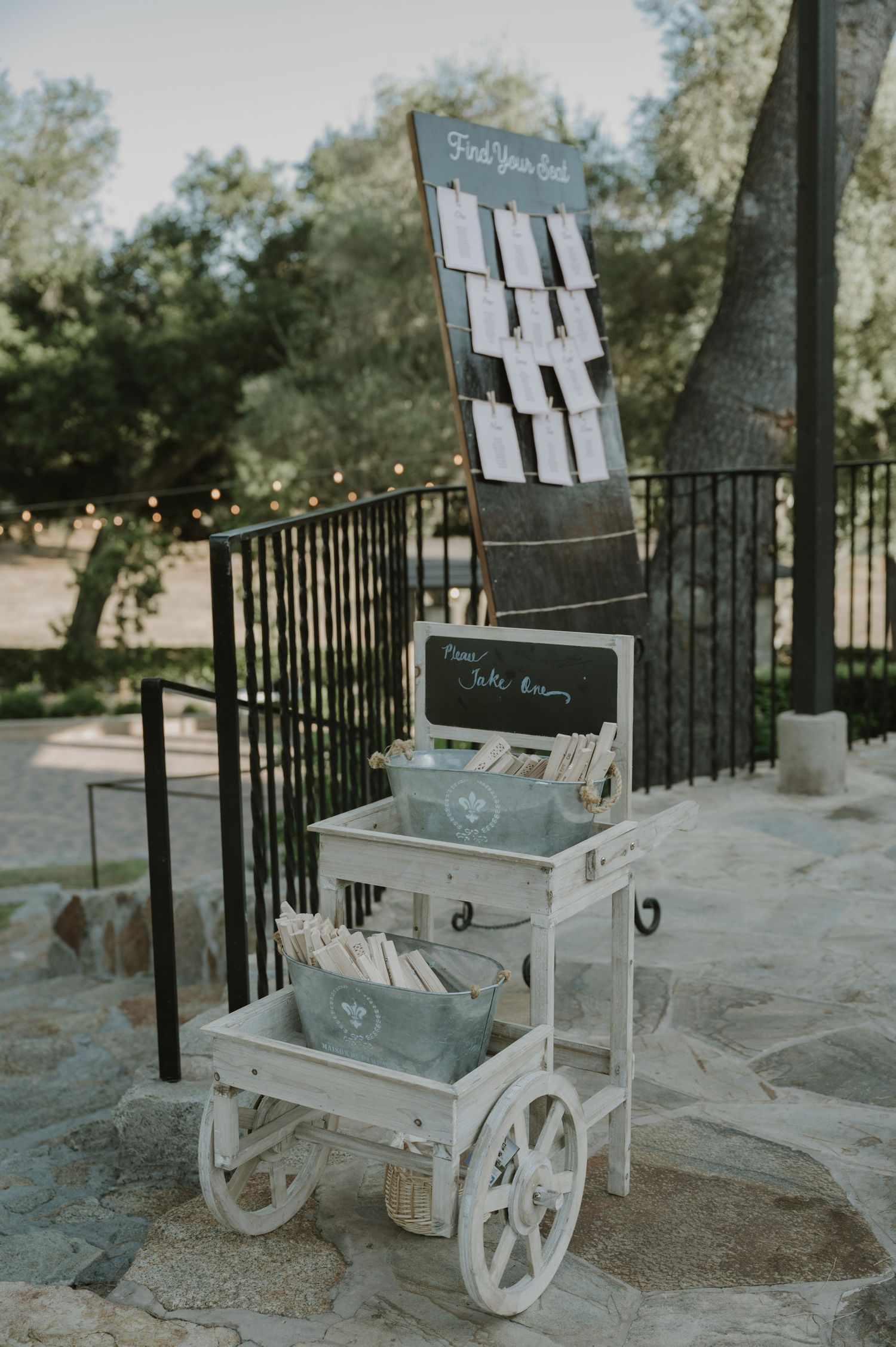 Rustic white wooden cart with seating chart and wedding programs at an outdoor venue.