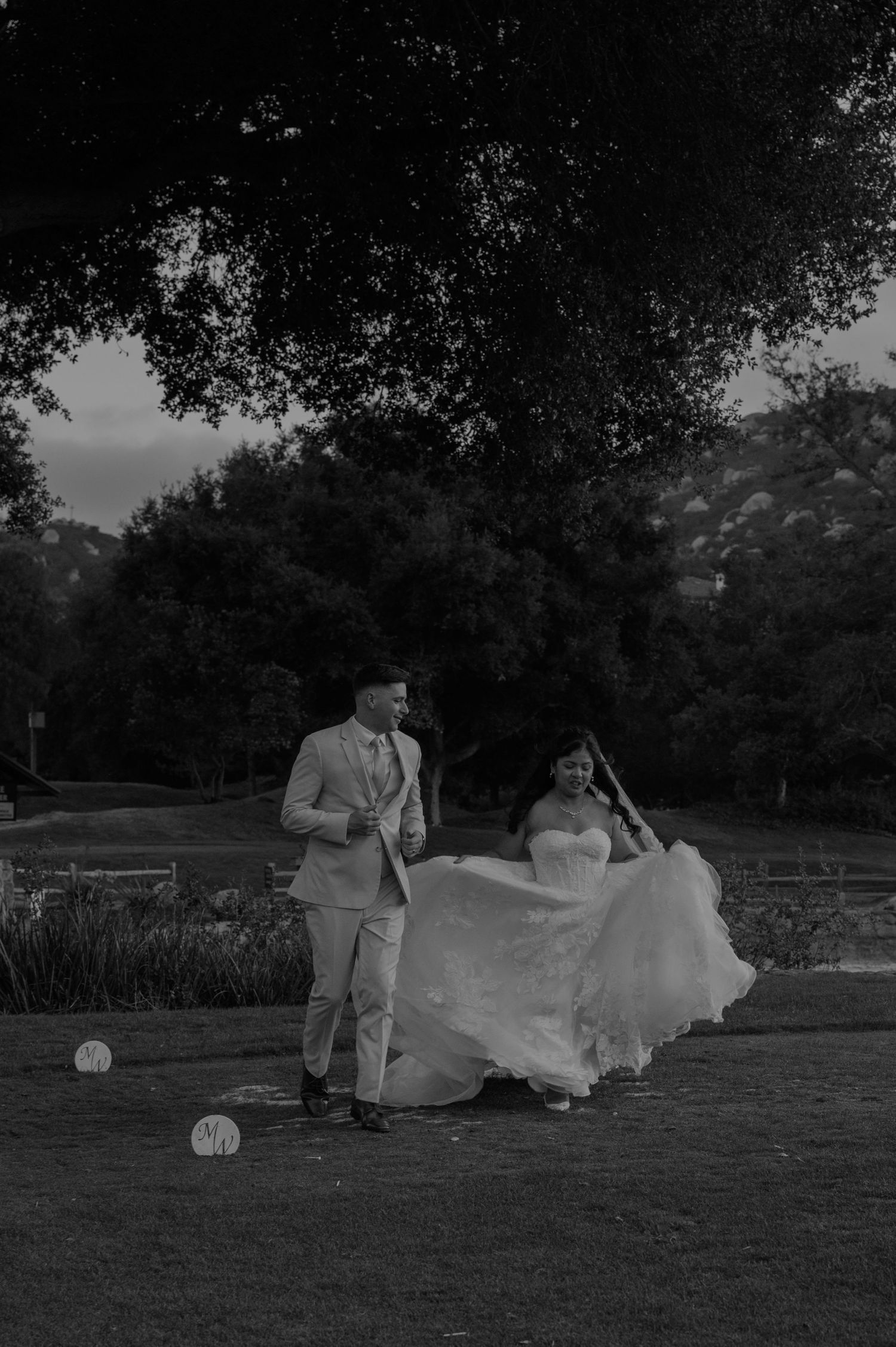 Bride and groom dancing outdoors under large trees in an elegant black and white wedding portrait.