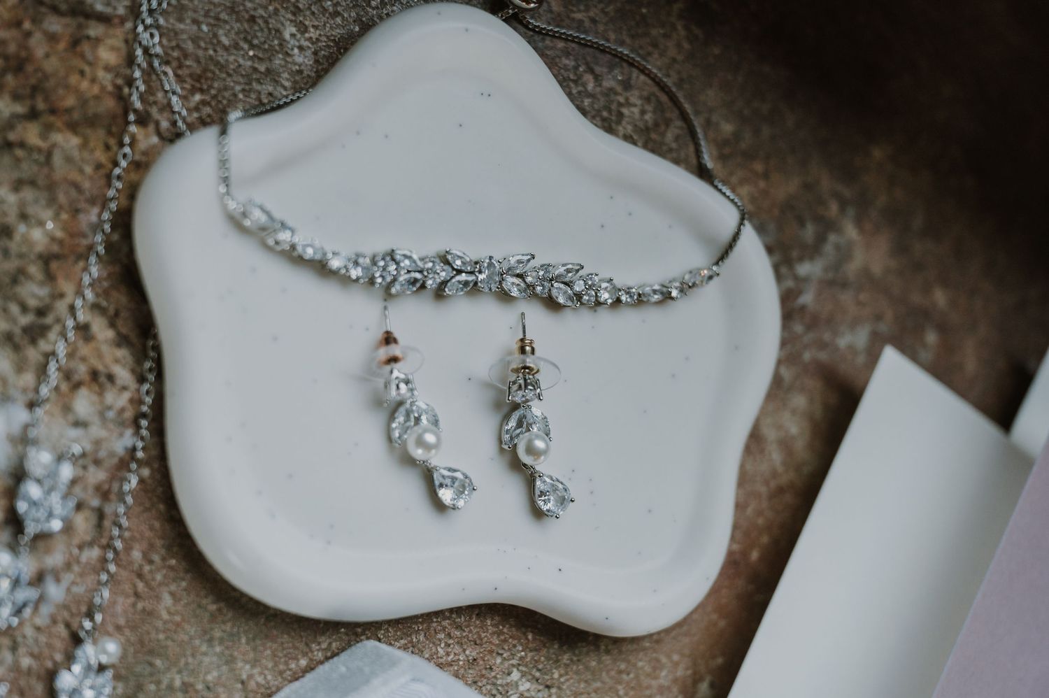 Elegant bridal jewelry set featuring a crystal headband and pearl drop earrings on a white dish.