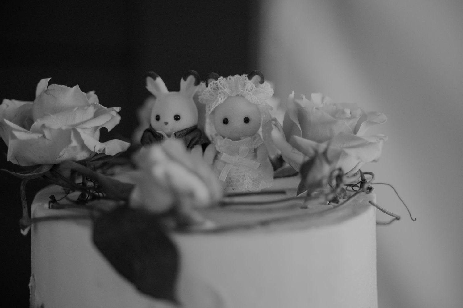 Black and white photo of cute bunny bride and groom cake toppers surrounded by roses on wedding cake.
