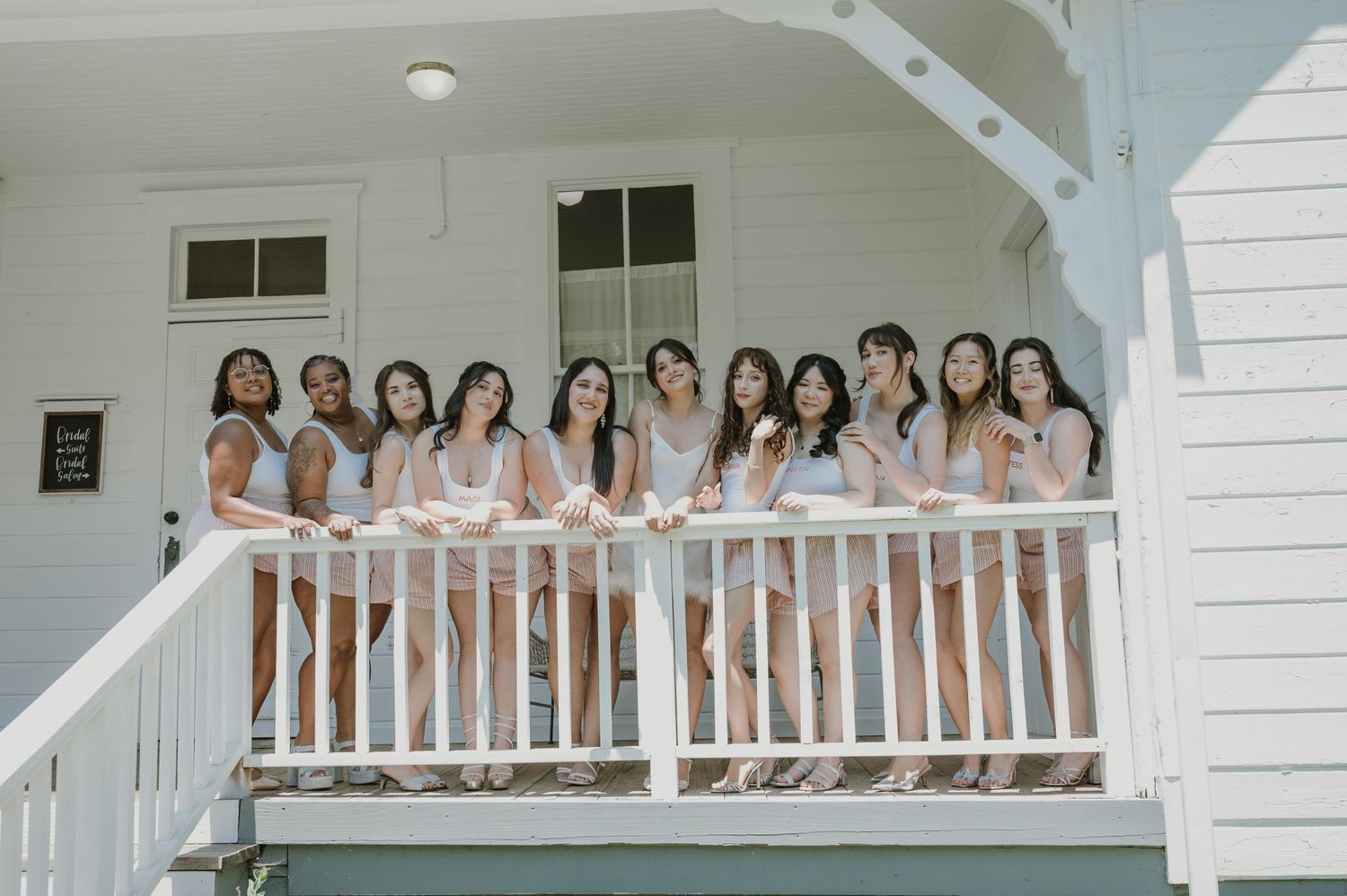 Group of bridesmaids in matching robes posing on a white porch railing.