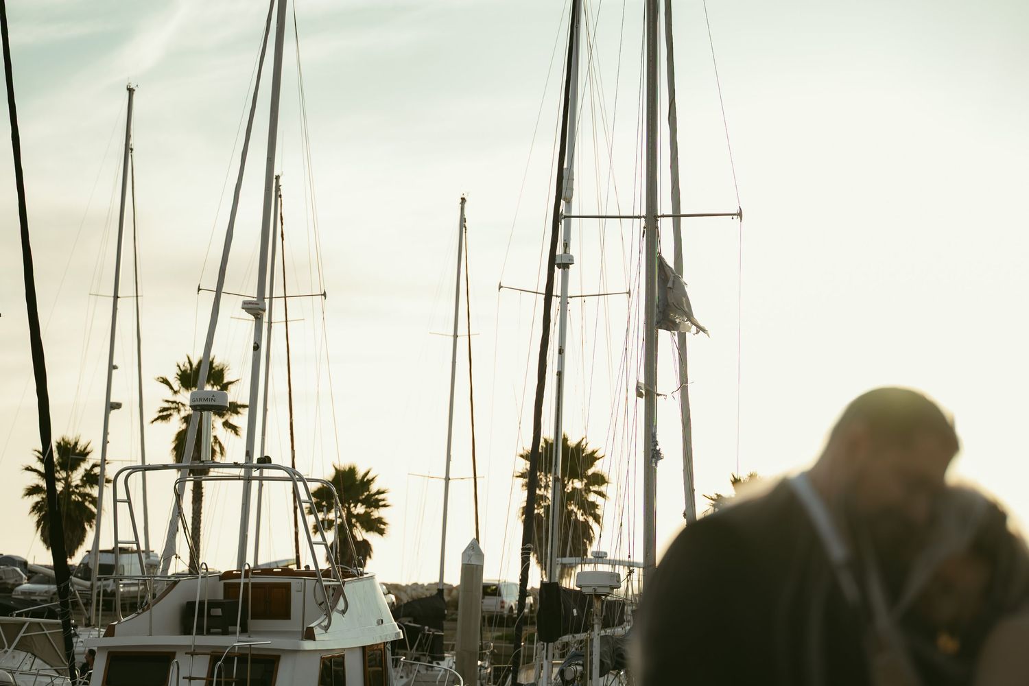 Bride and groom sharing a kiss at golden hour with sailboats and palm trees in the background.