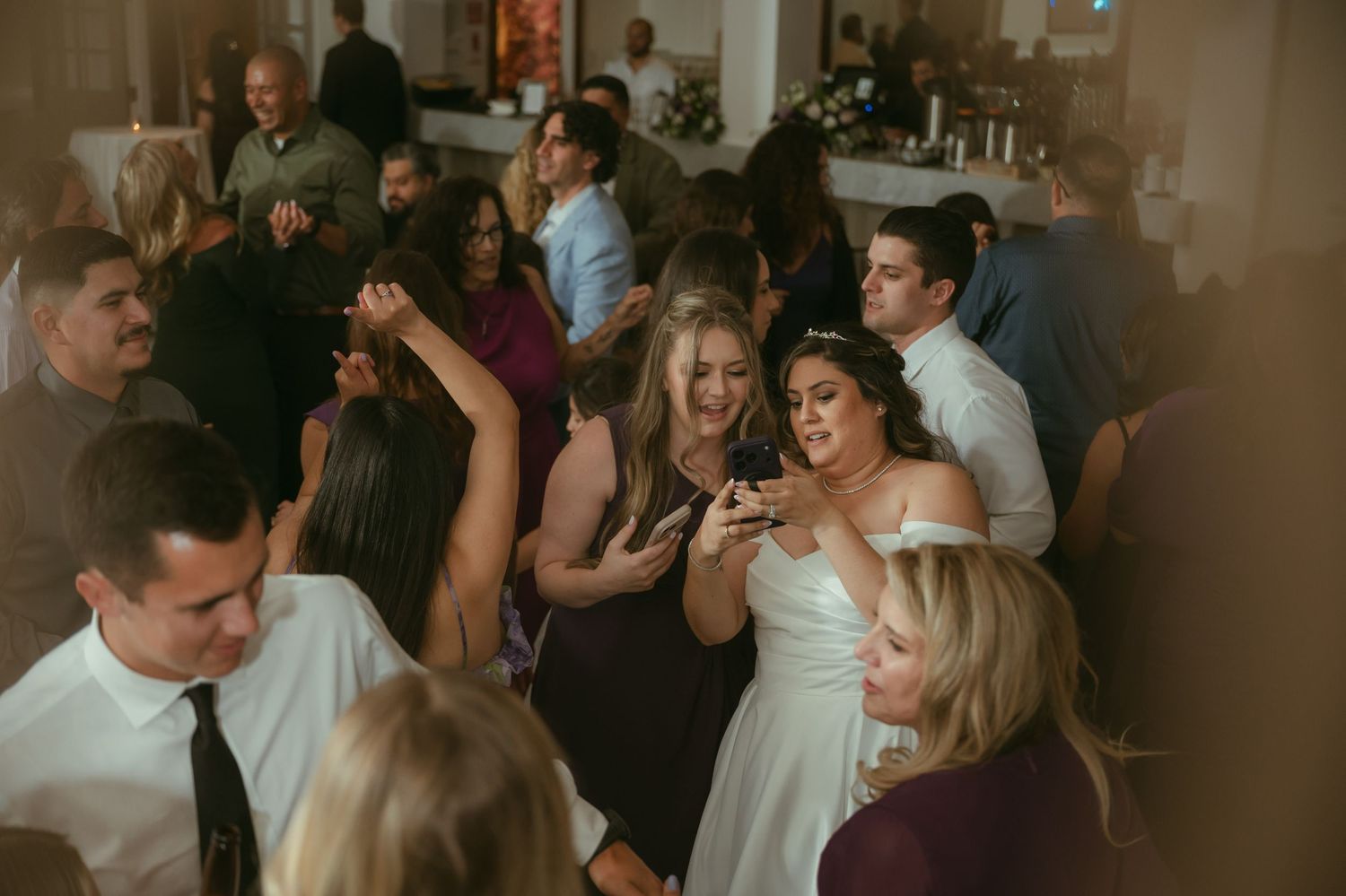 Wedding guests dancing and celebrating on the dance floor at a lively indoor wedding reception.