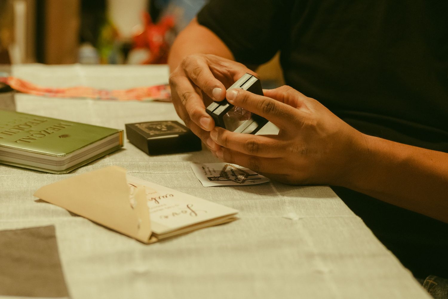 Person examining small items at a table with books and papers during an indoor gathering.
