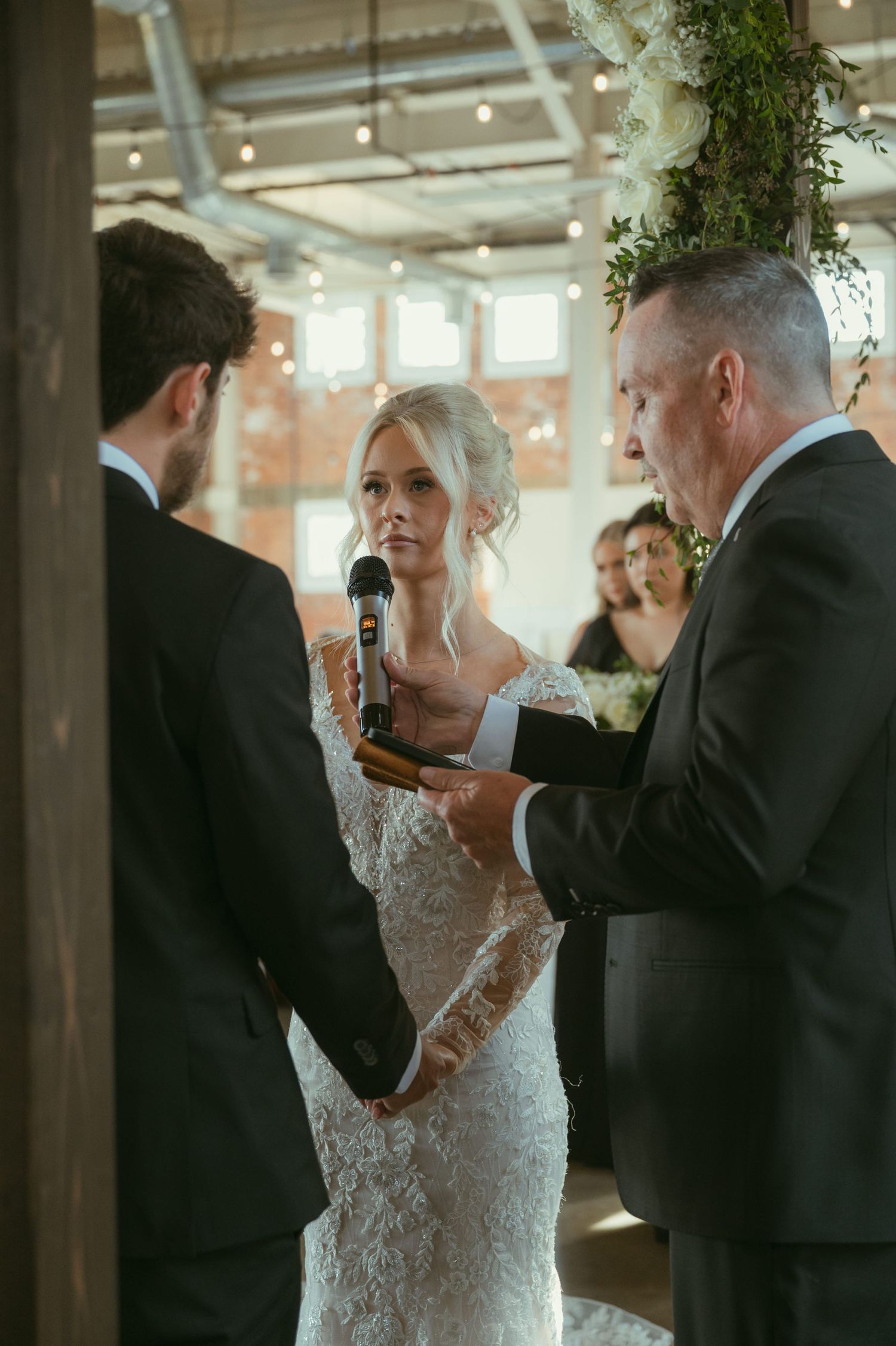 Bride listens attentively as officiant reads vows during elegant indoor wedding ceremony.