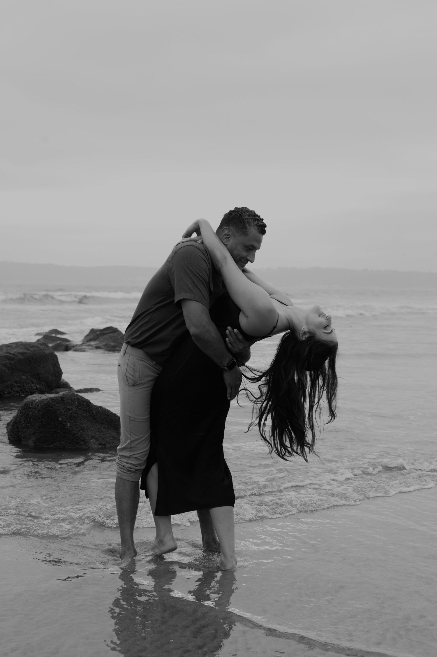 Couple playing in the ocean waves during a cloudy day photoshoot.