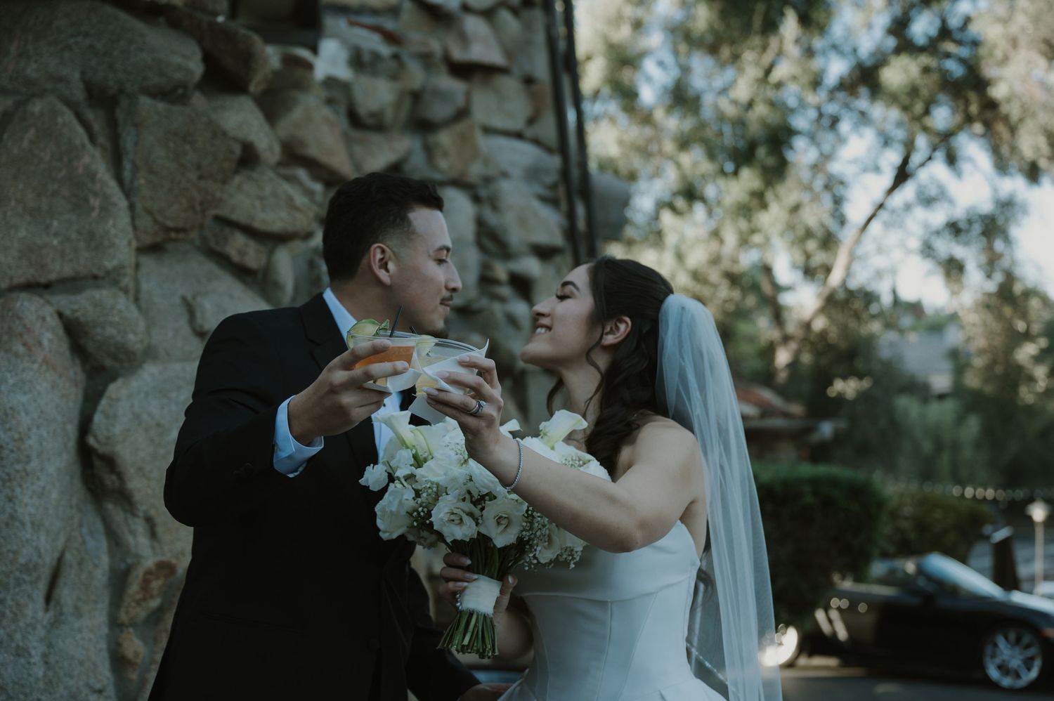 Newlyweds share a moment with bouquet outside stone building during wedding celebration.