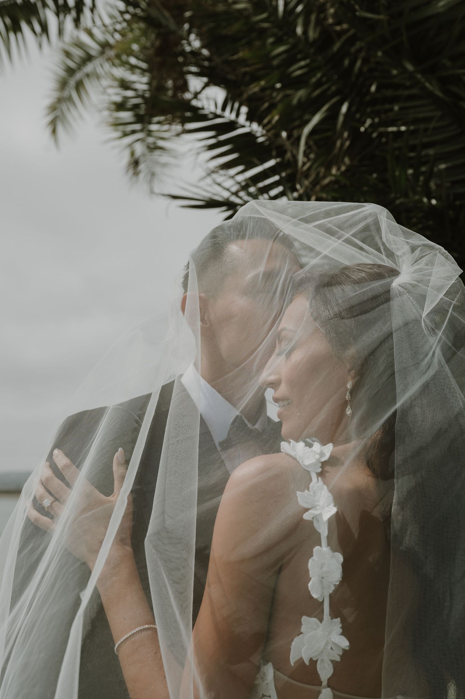 An artistic wedding photo with a delicate veil flowing between a couple during an intimate moment.