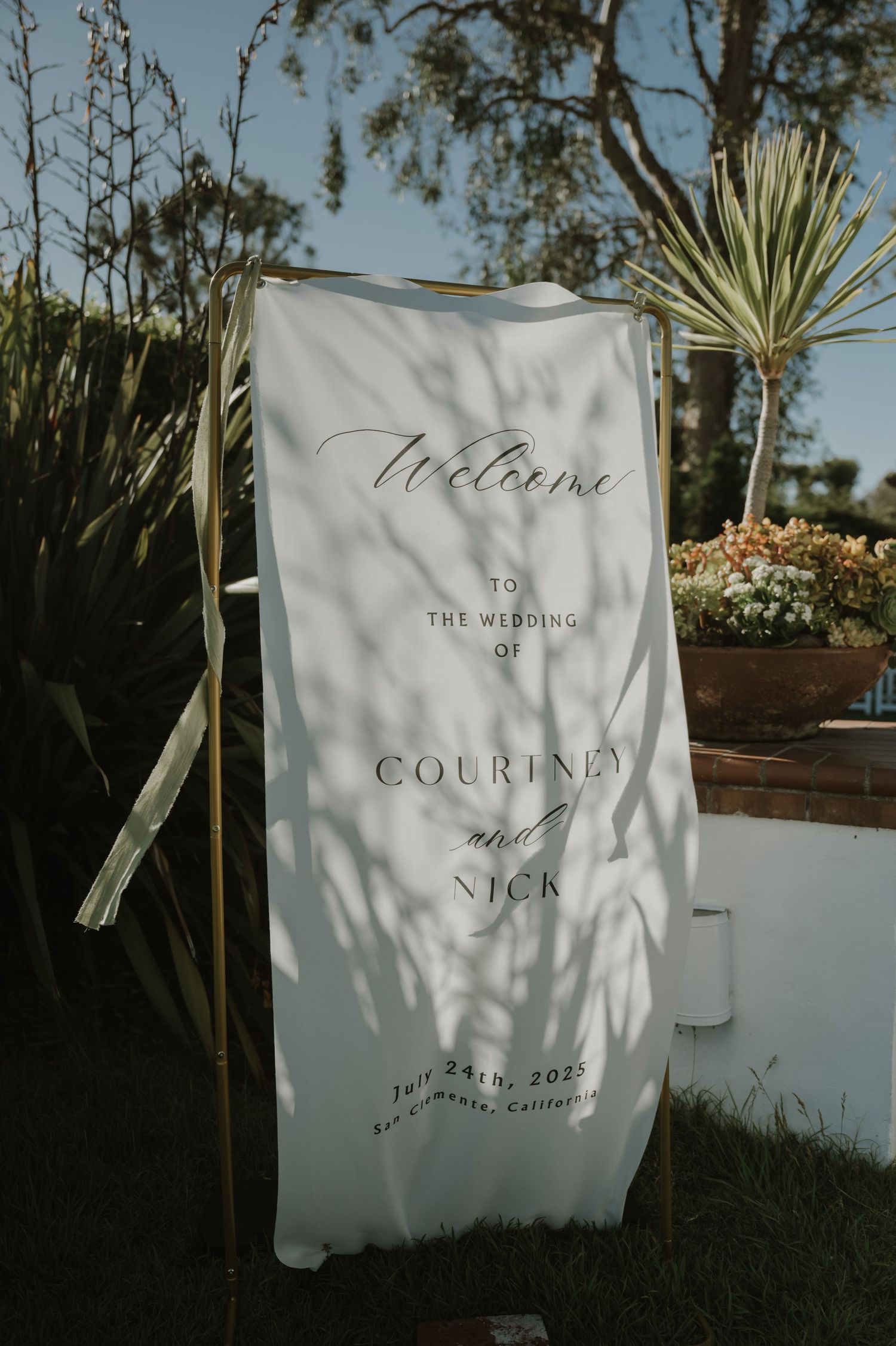 Elegant white wedding welcome sign for Courtney and Nick, July 24th 2025, San Clemente California, displayed outdoors.