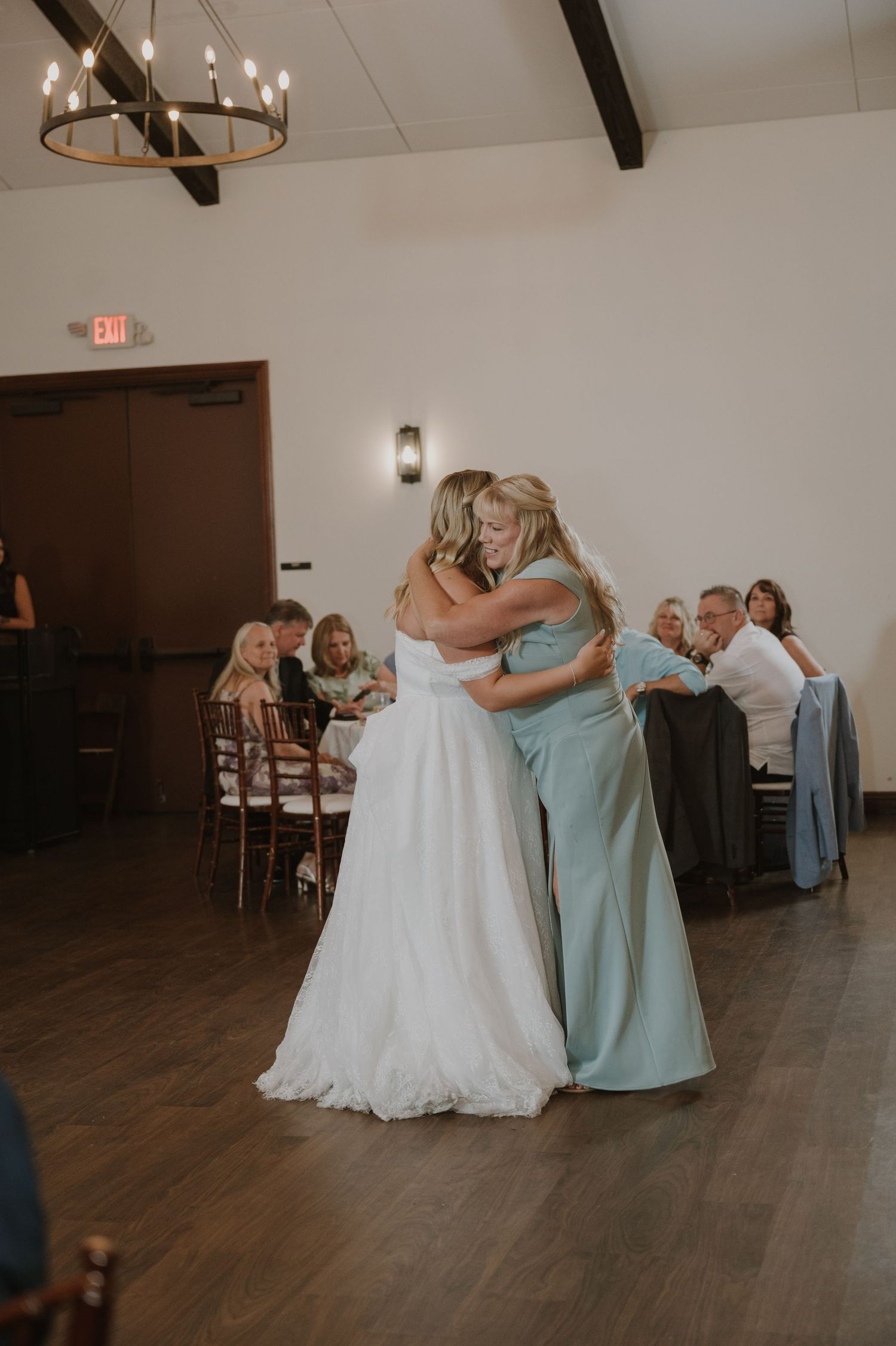 Bride and guest share an emotional hug on the dance floor during a wedding reception in an elegant venue.