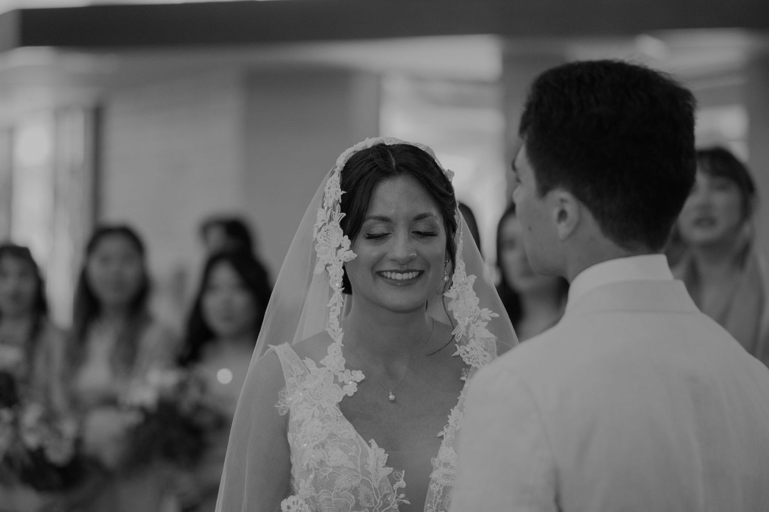Radiant bride smiles at groom during wedding ceremony in black and white portrait photo.
