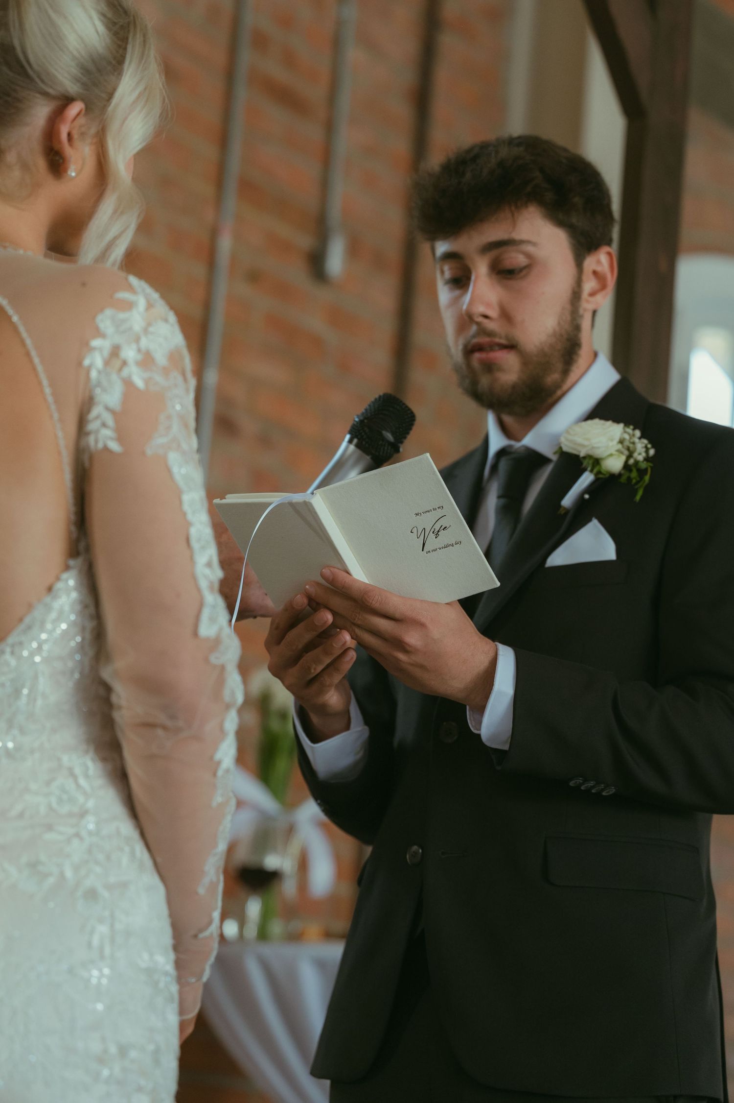 A groom in a black suit reads wedding vows from a book at the altar during a wedding ceremony.