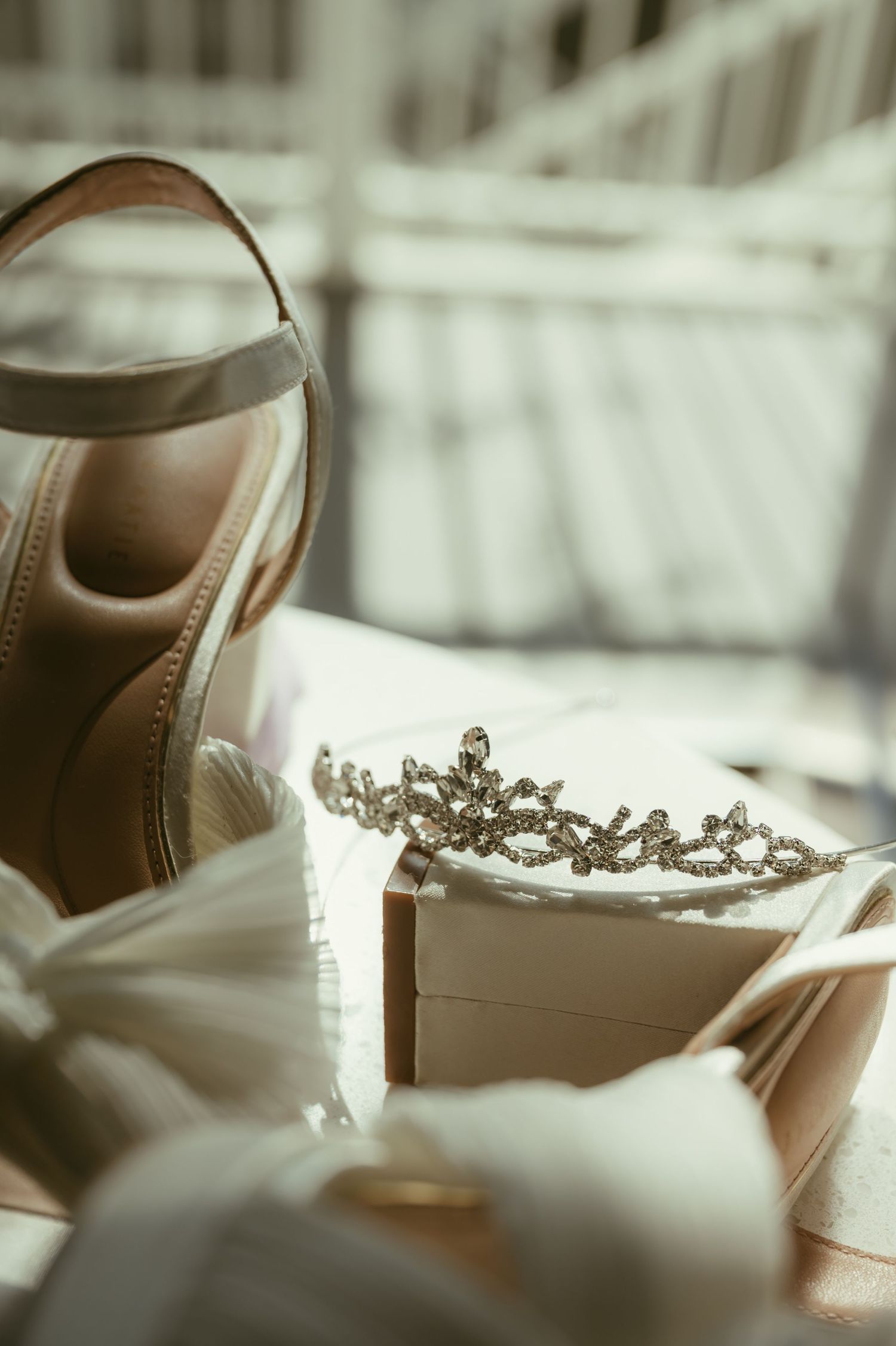 Bridal accessories flat lay featuring nude heeled sandals, a crystal tiara, and a white clutch purse.
