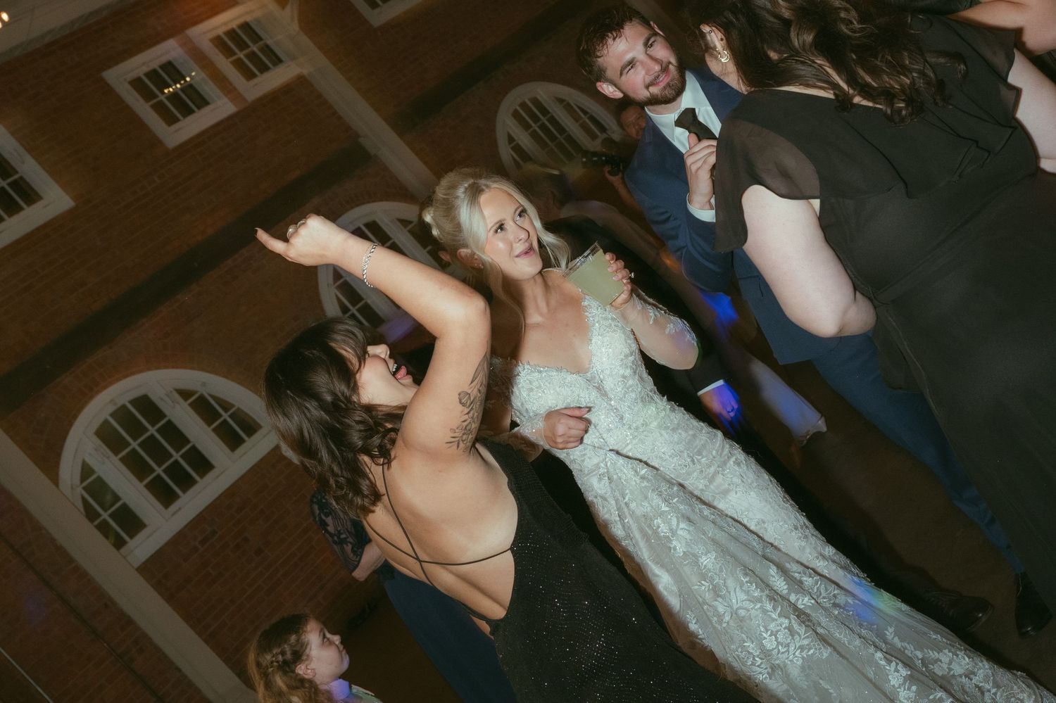 Bride in lace gown dances joyfully with guests on the wedding reception dance floor.