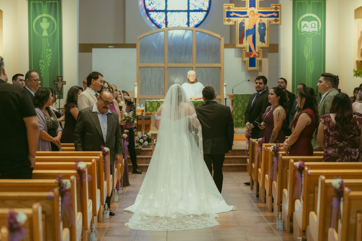 Bride in white gown and veil walks down church aisle toward altar during wedding ceremony.