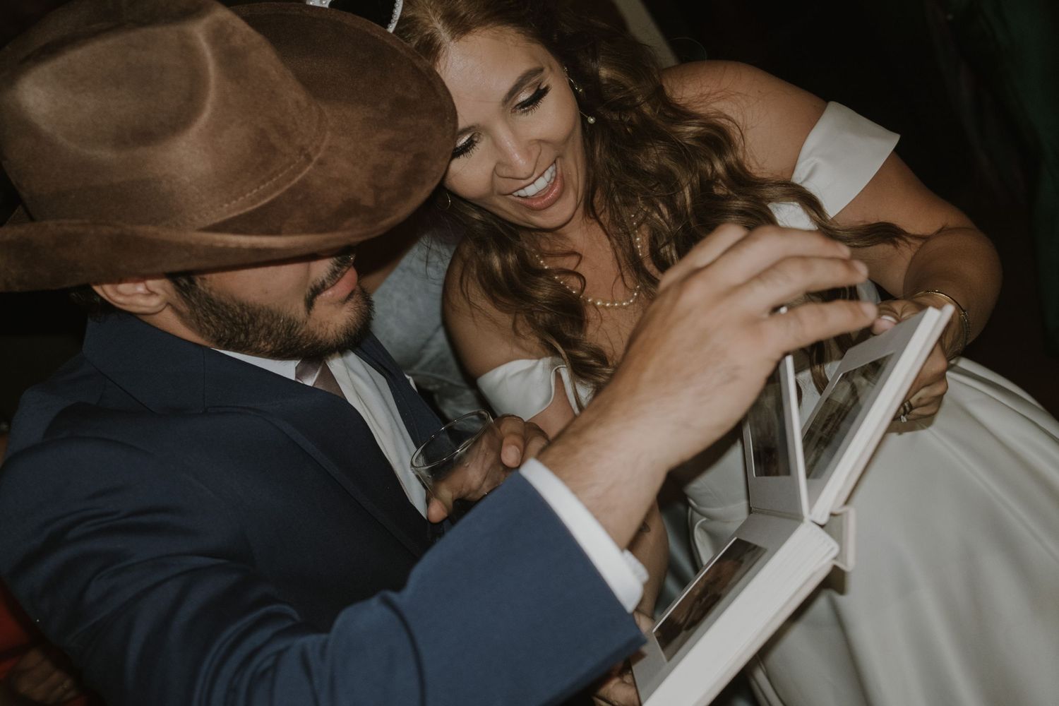 Smiling bride in white dress laughing with cowboy hat wearing guest at wedding reception.