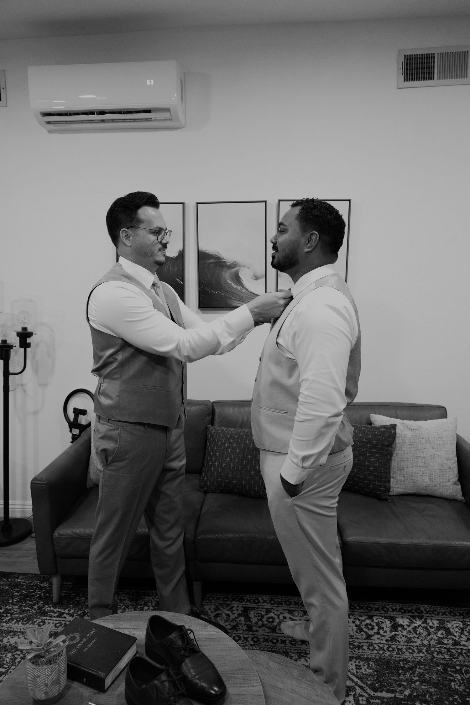Black and white photo of two grooms helping each other get dressed before their wedding ceremony.