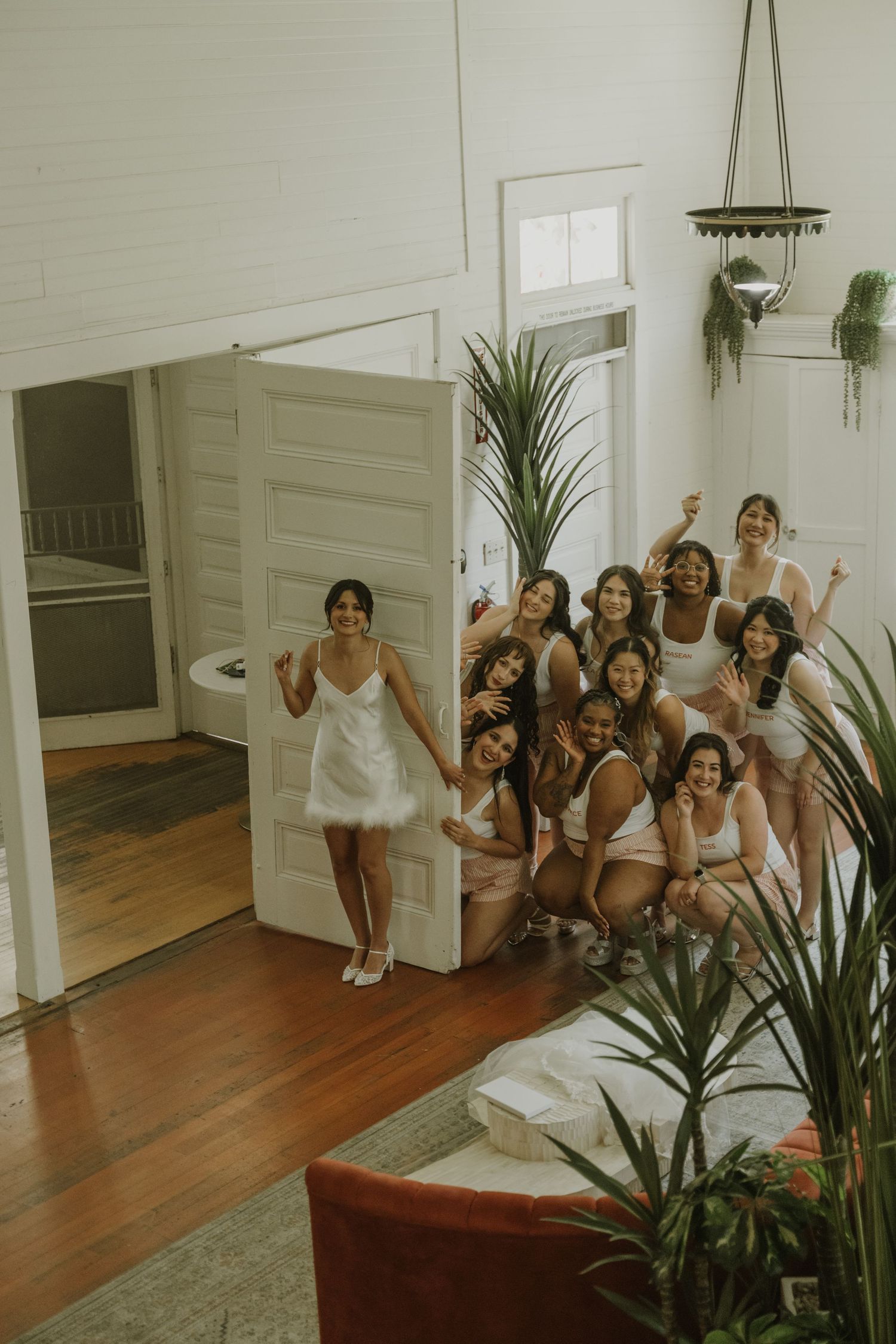 Aerial view of bride in white dress posing with bridesmaids in a bright white room.