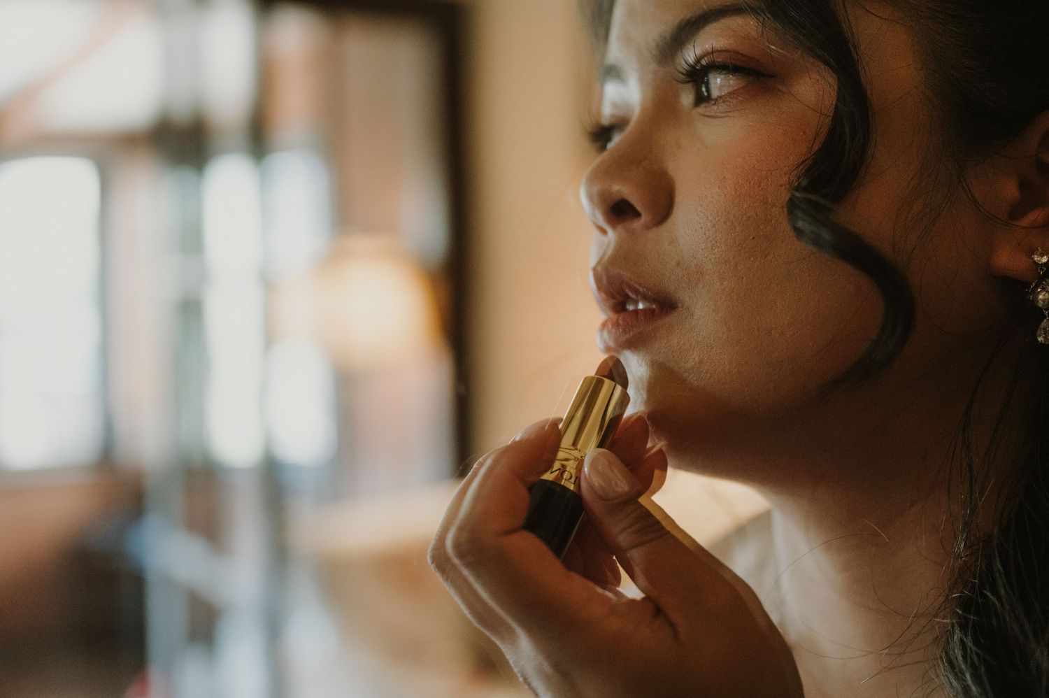 Close-up of bride applying red lipstick during wedding day bridal preparations.
