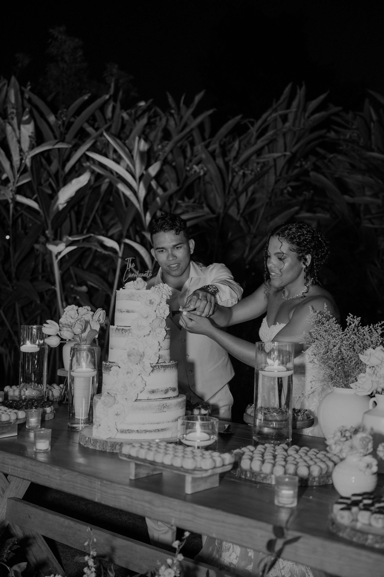 Couple cutting wedding cake at dessert table in black and white photo.