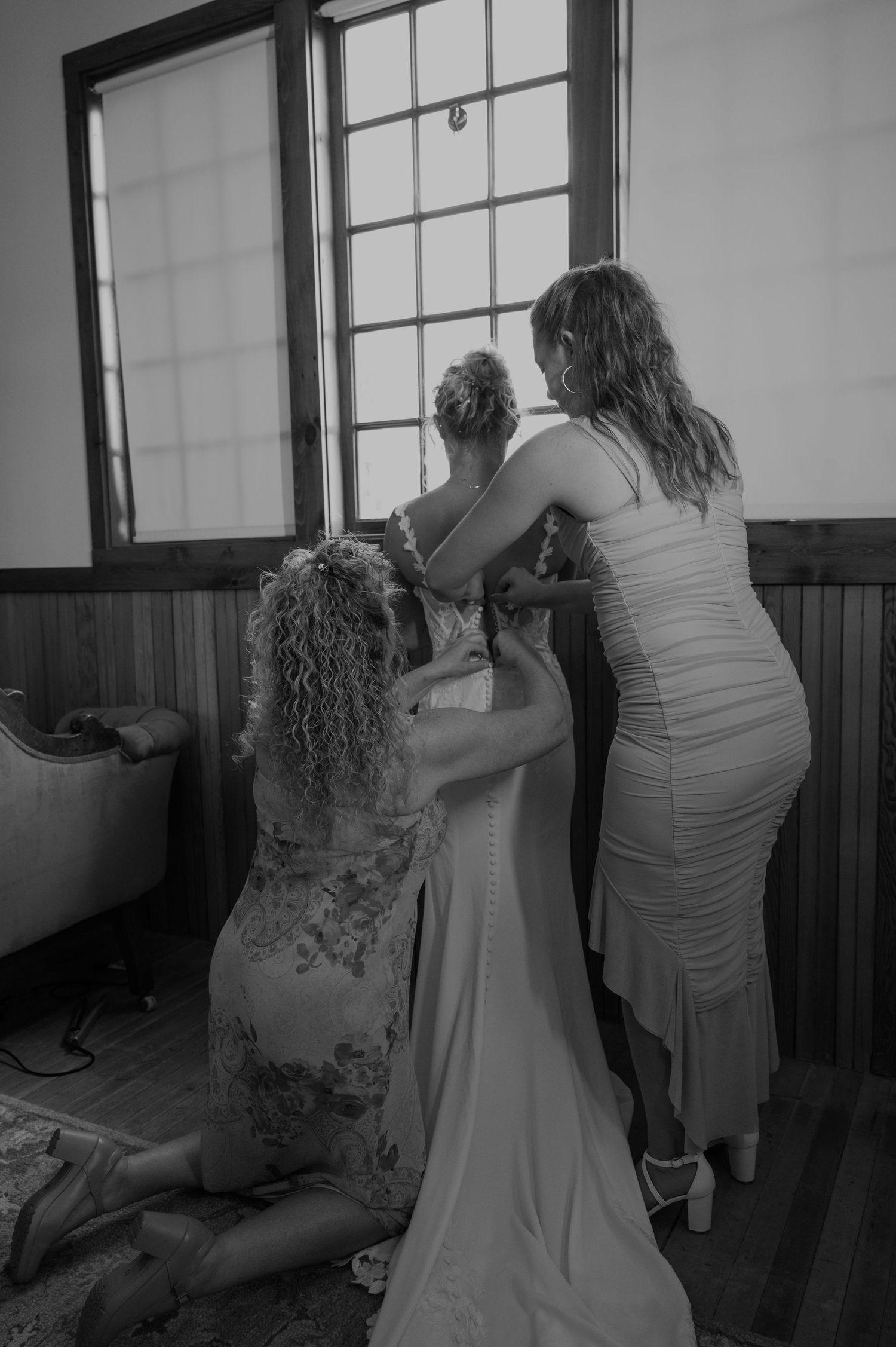 Black and white photograph of wedding preparation moments near large windows.