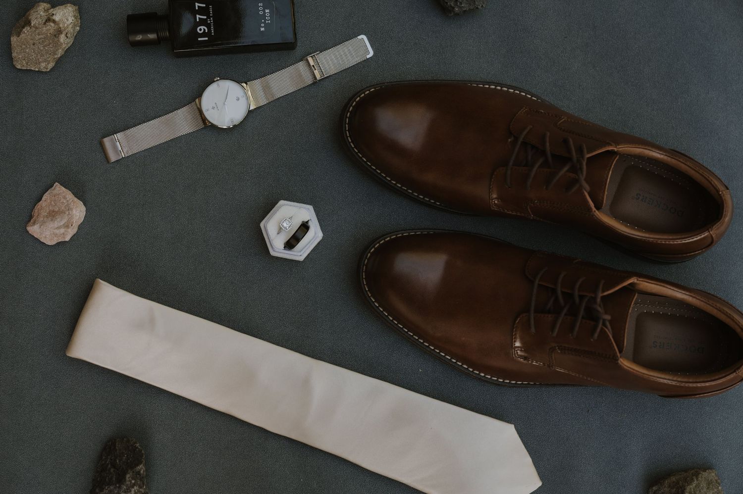 Brown leather dress shoes and accessories arranged on a dark surface.