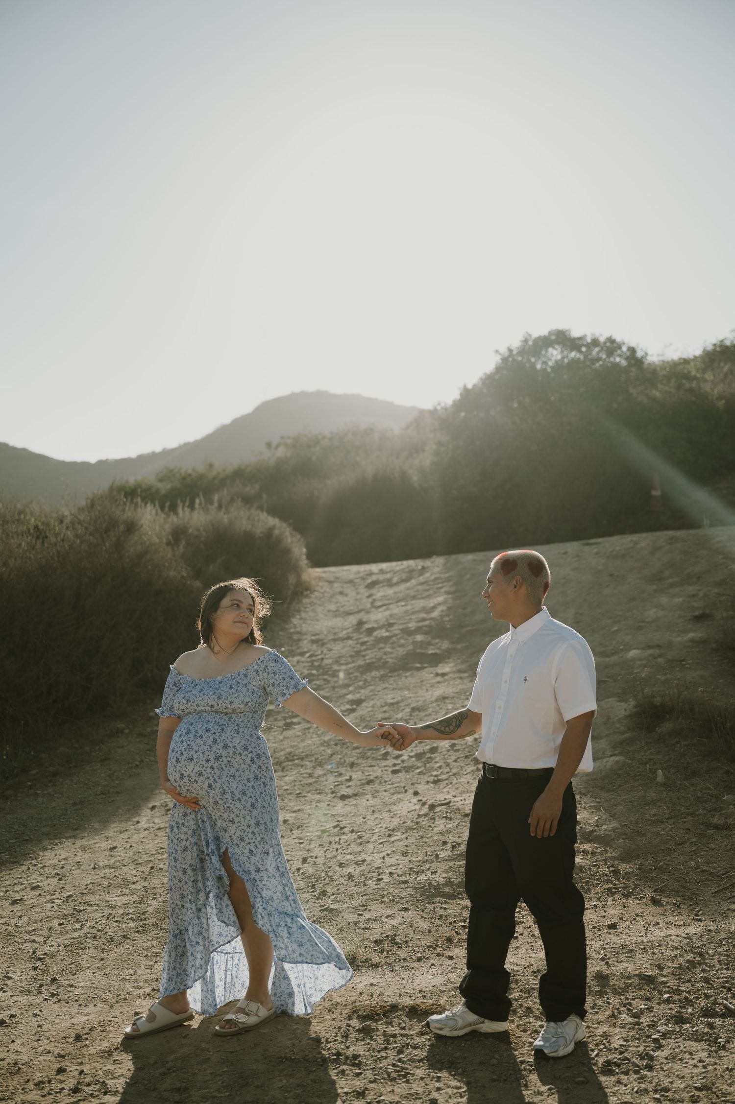 A couple shares a tender moment on a mountainside trail at sunset.
